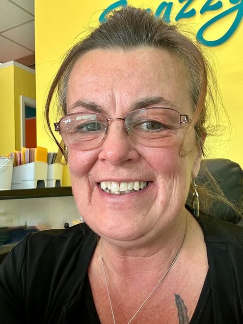 Woman with glasses smiles, standing in front of yellow background.