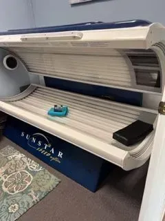 A Sunstar tanning bed in a room with a blue base and white top.