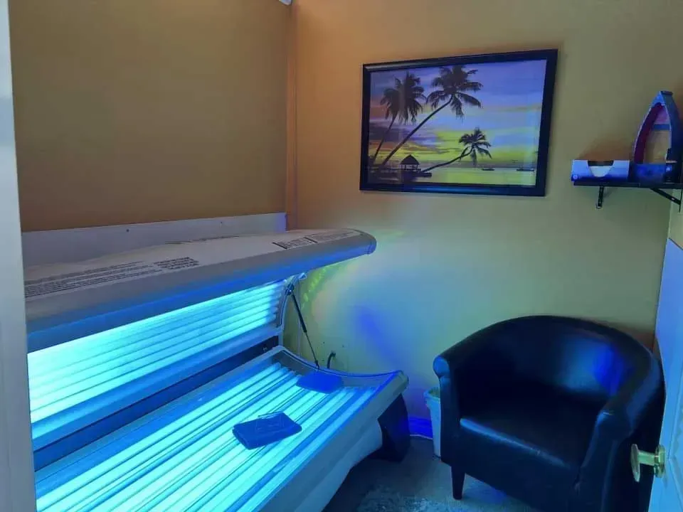 Tanning bed room with blue lights, a black chair, and palm tree art on the wall.