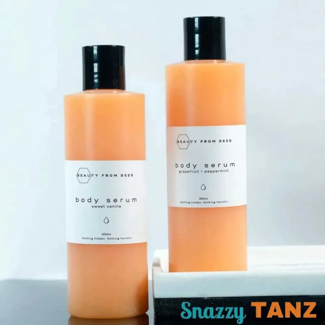 Two bottles of orange body serum with black caps and white labels, on a white surface.