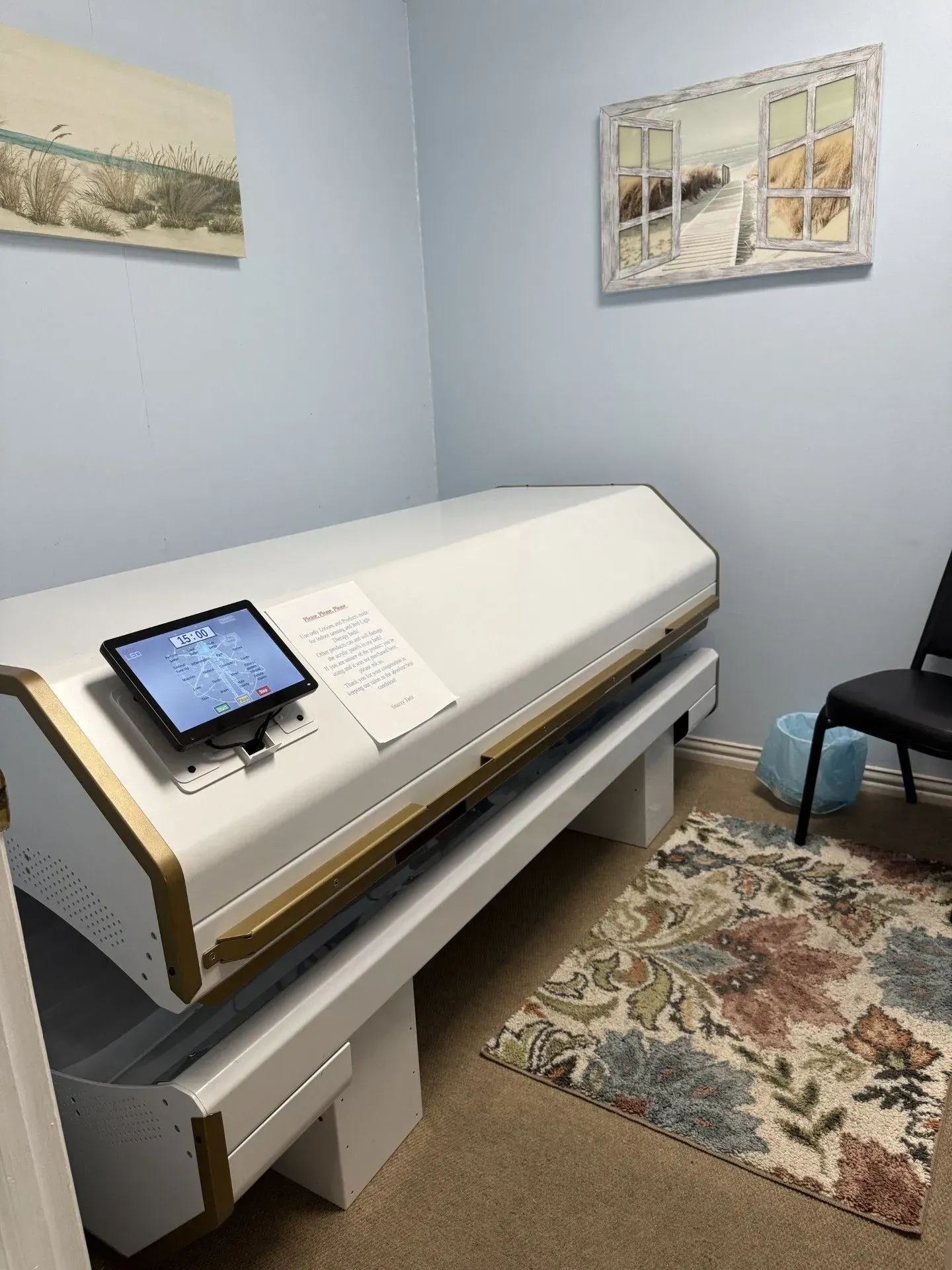 A white, coffin-shaped hyperbaric chamber in a room with artwork and a floral rug.