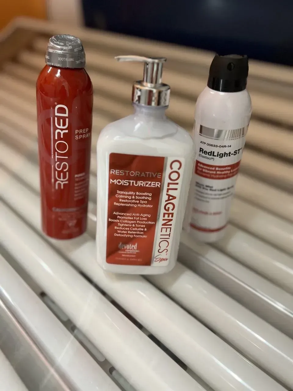 Three skincare products: red spray, white lotion with pump, white spray on a tanning bed.