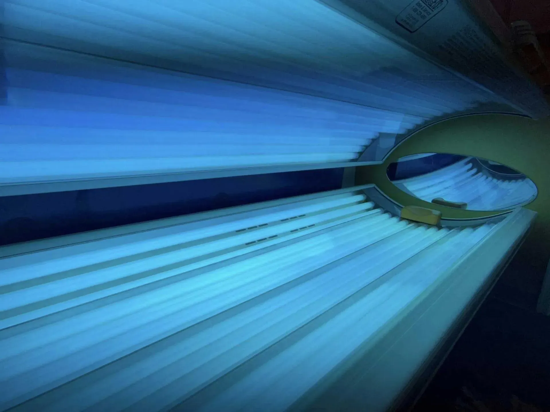 Tanning bed interior, bright blue light radiating from fluorescent bulbs, angled view.
