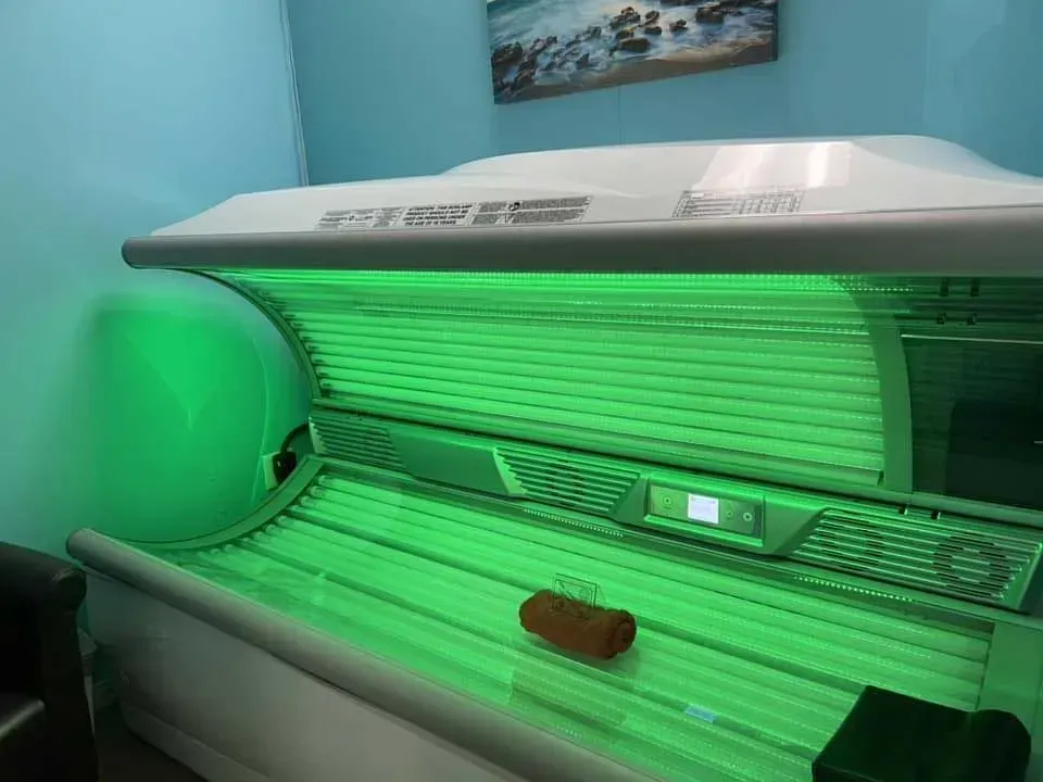 Tanning bed with green lights on in a blue-walled room.