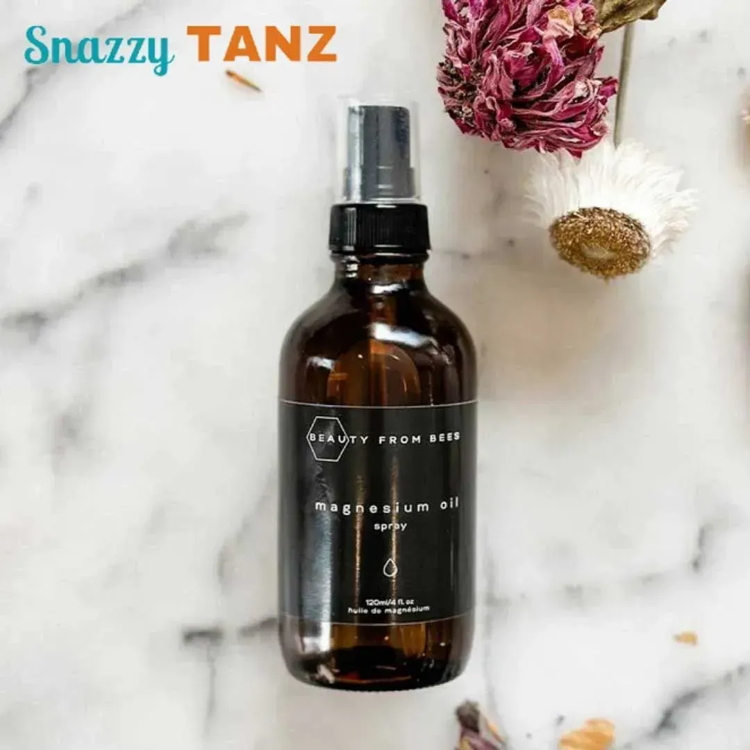 A dark brown bottle of body oil with a spray nozzle on a marble surface with flowers.