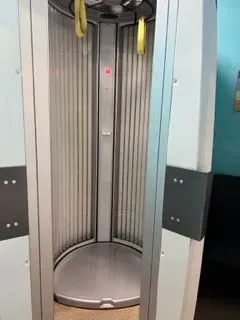 A stand-up tanning bed with a silver interior, yellow handles, and gray exterior panels.