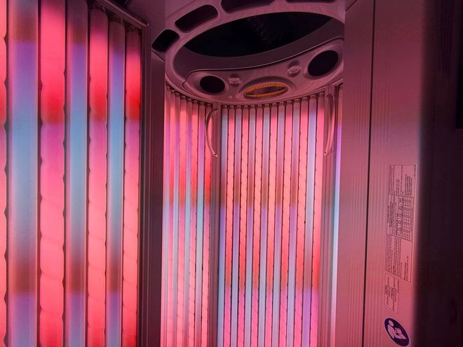 Tanning bed interior illuminated with red and pink lights.