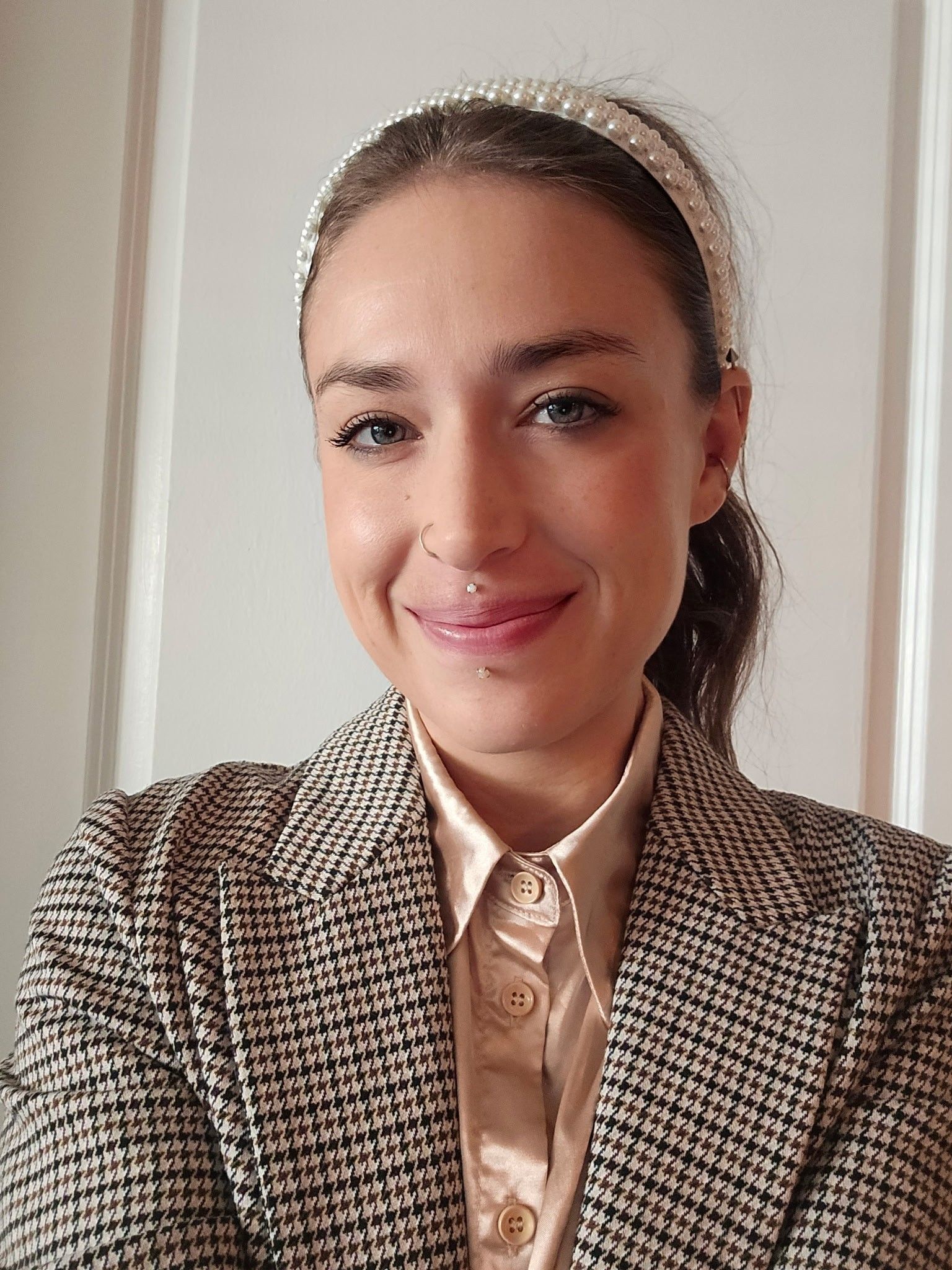 Woman with pearl headband, blazer, smiling at the camera.