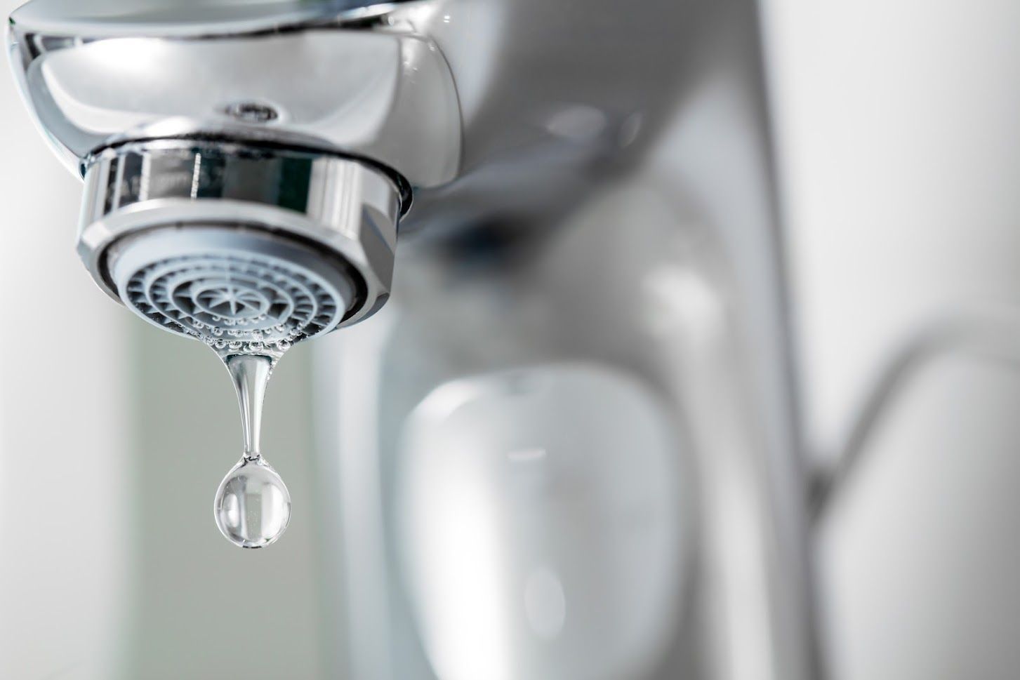 A close-up of a shiny metal faucet dripping a single, clear water droplet from its aerator.