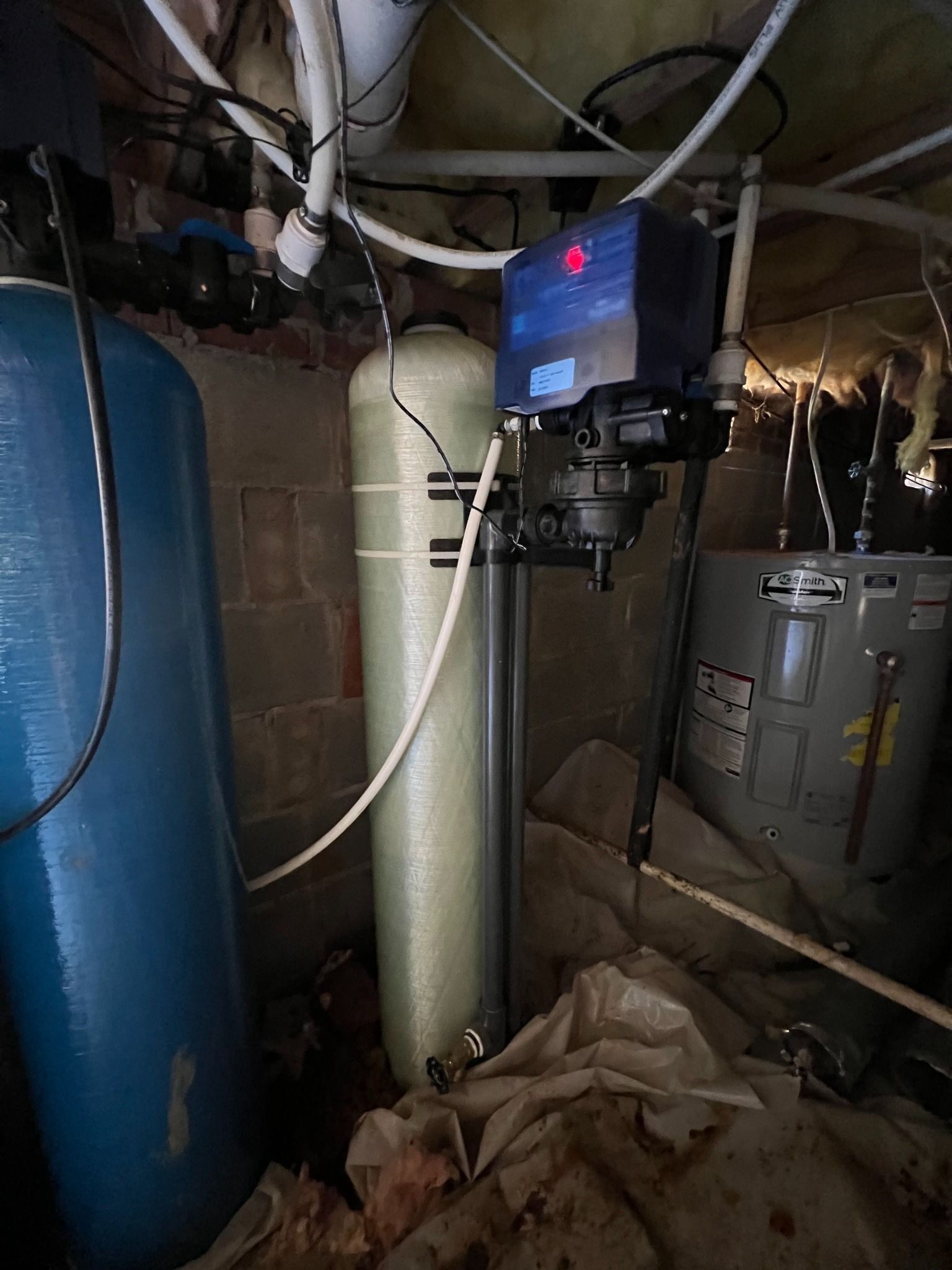 Water treatment equipment with a blue tank, a beige filtration tank, and a control head in a residential basement.