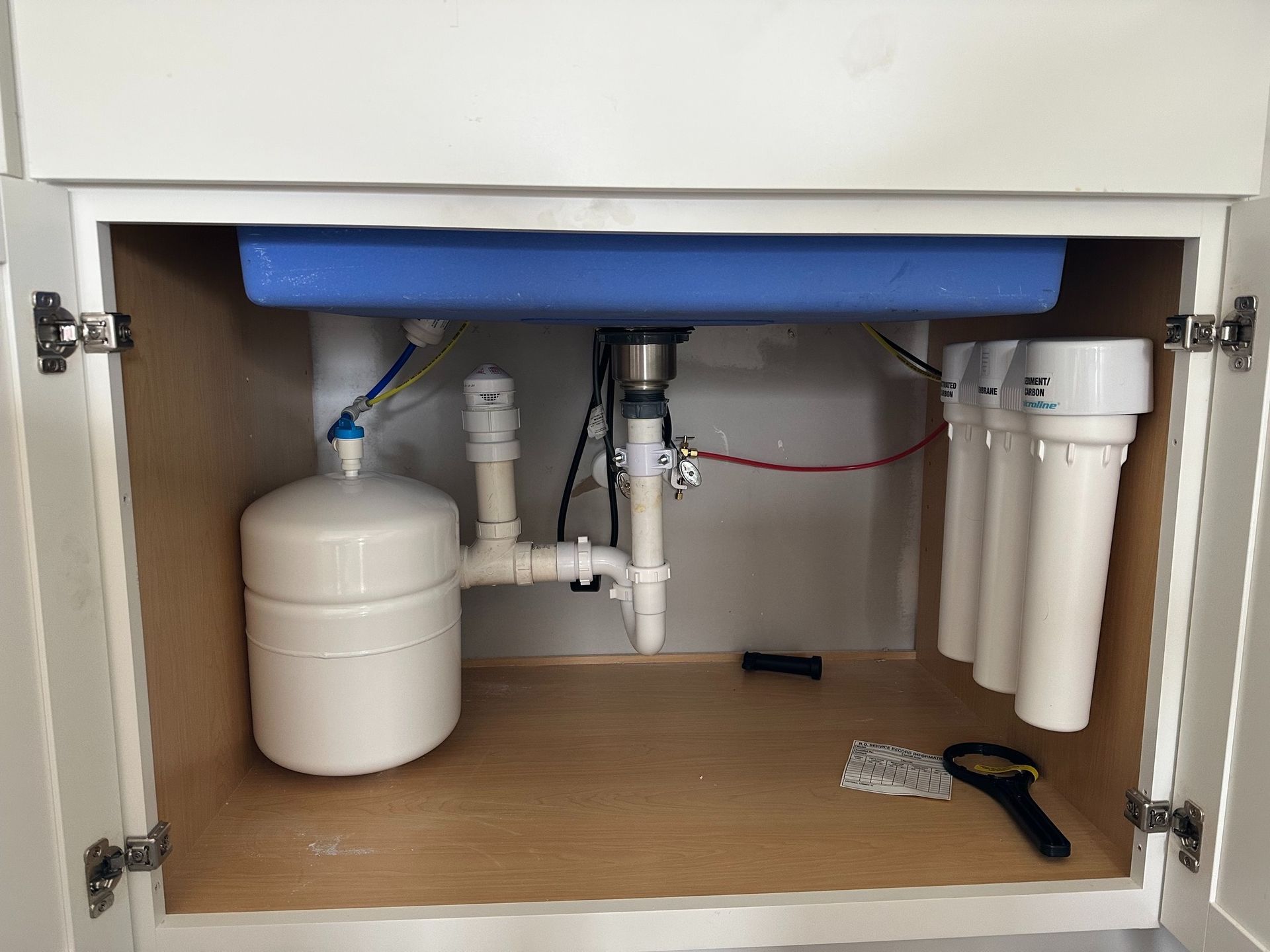 Under-sink reverse osmosis water filtration system with a white storage tank and three vertical filter cartridges.