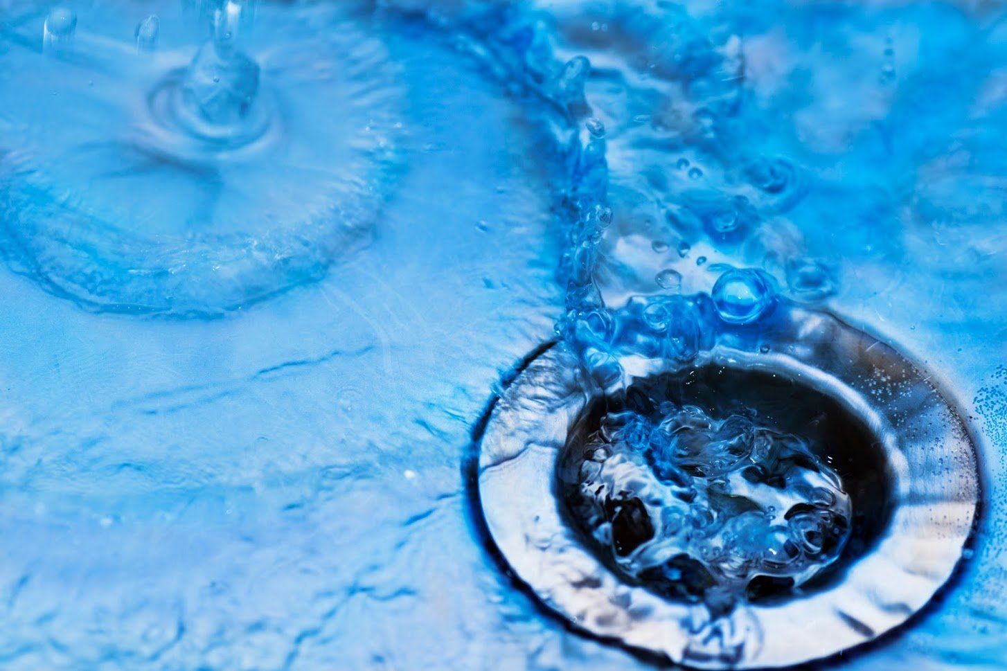 Water flows over a chrome drain in a bright blue sink.