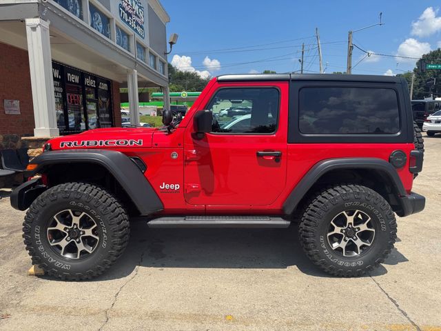Red two-door Jeep Wrangler parked outside a storefront, with black hardtop and off-road tires.