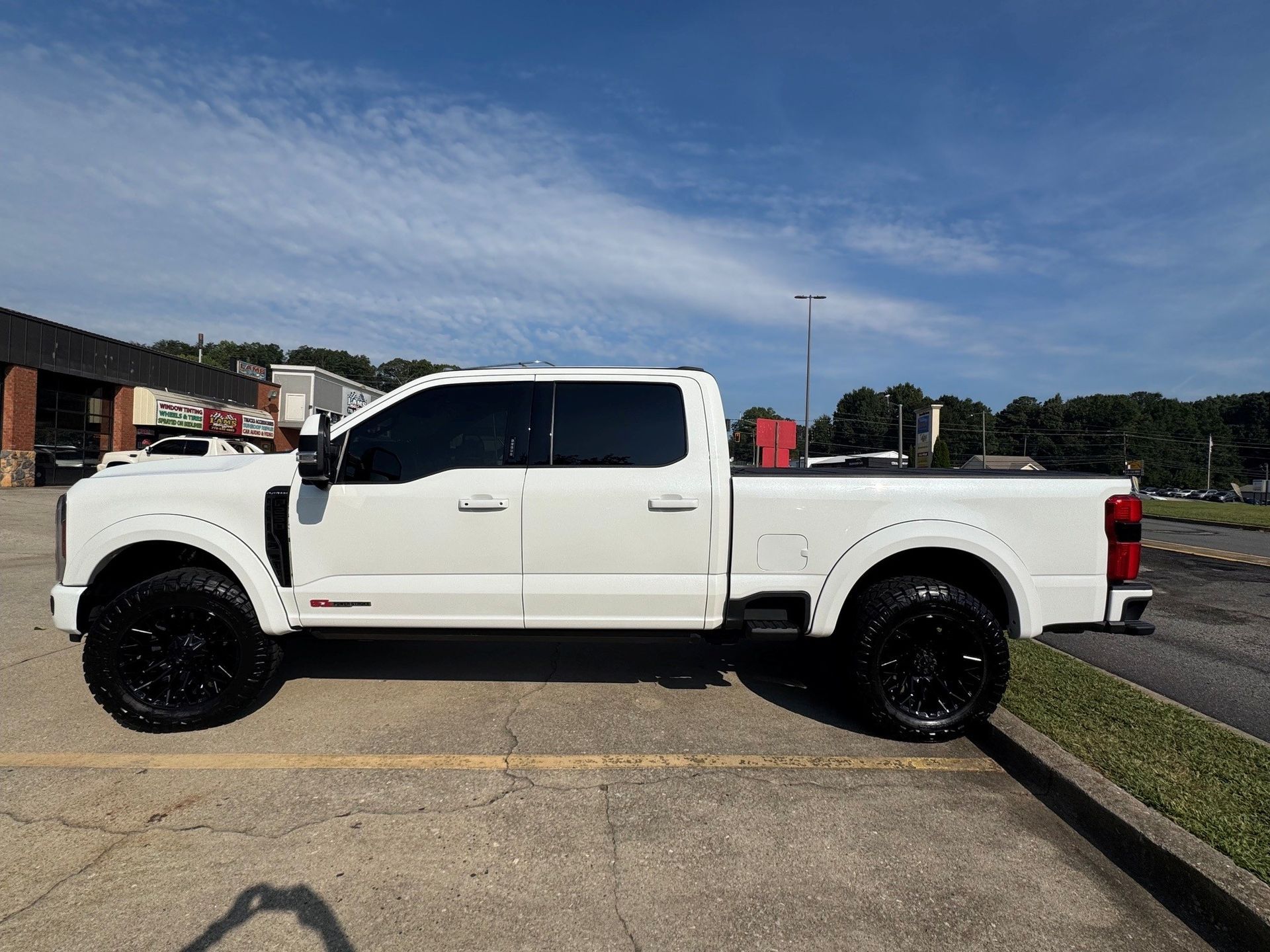White crew cab pickup truck parked on a sunny roadside, side view
