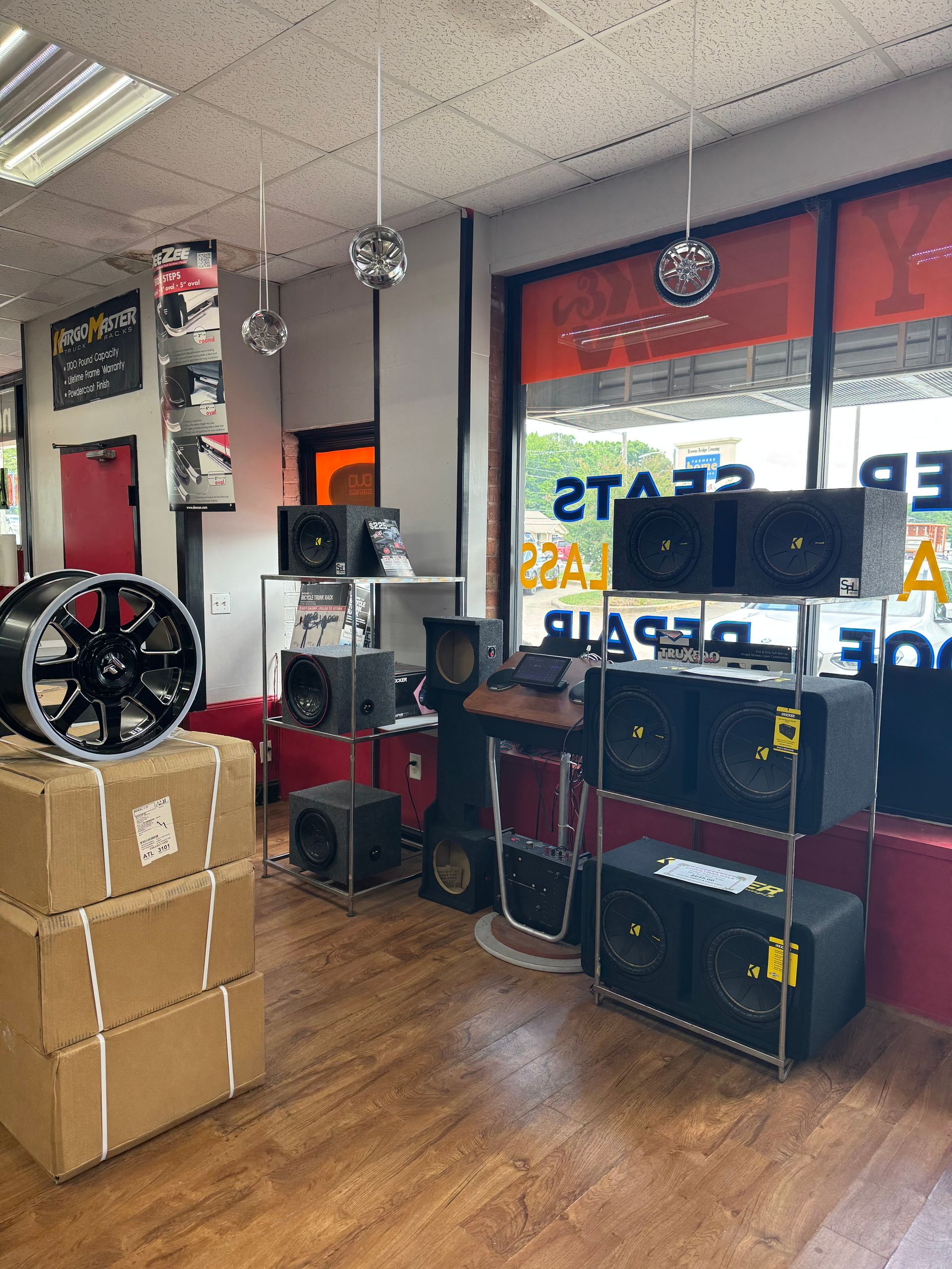Wheel display and stacked boxes inside an automotive shop with shelves and a window sign.