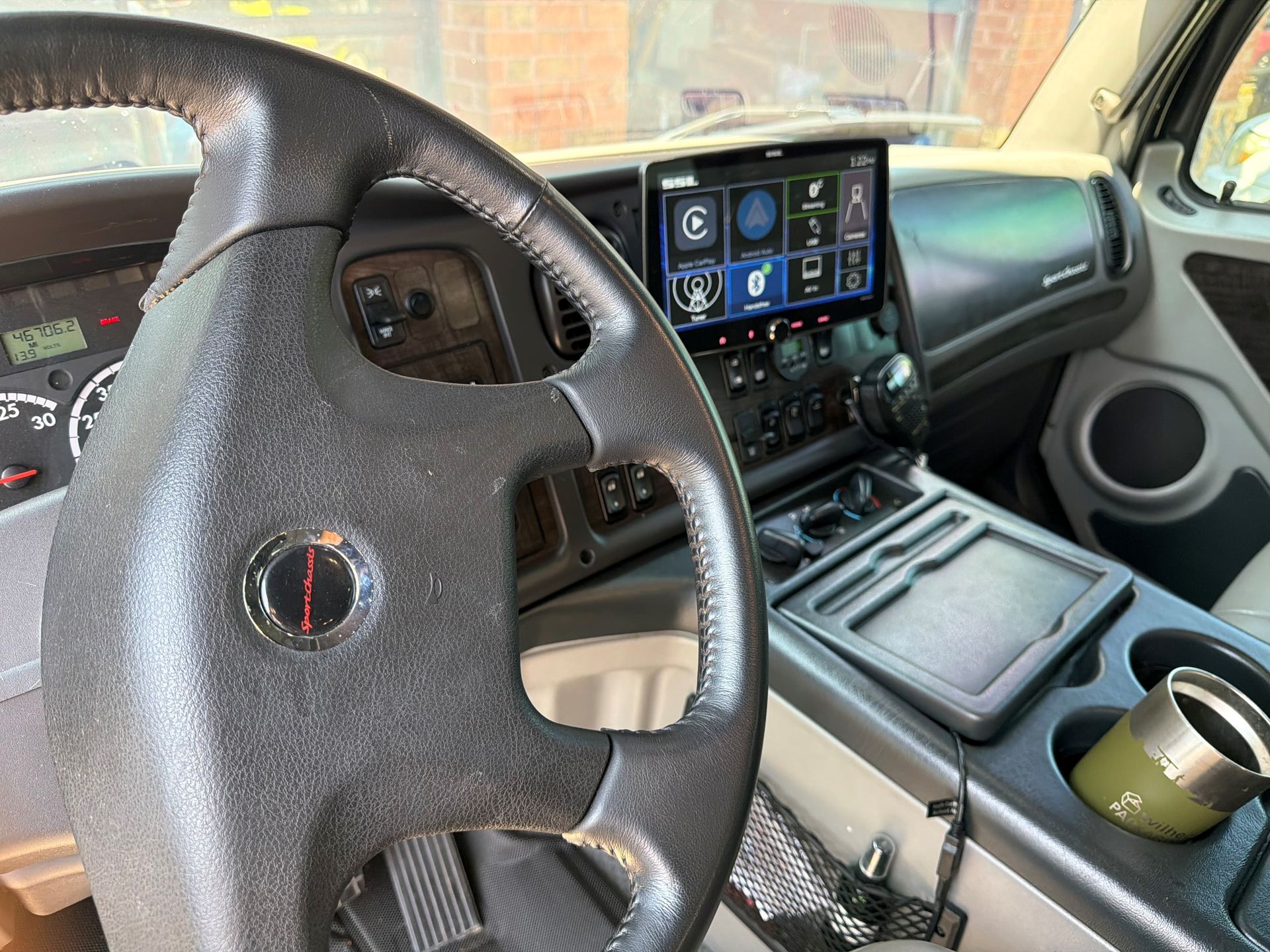 Car interior with steering wheel, dashboard screen, center console, and cup holder with a drink