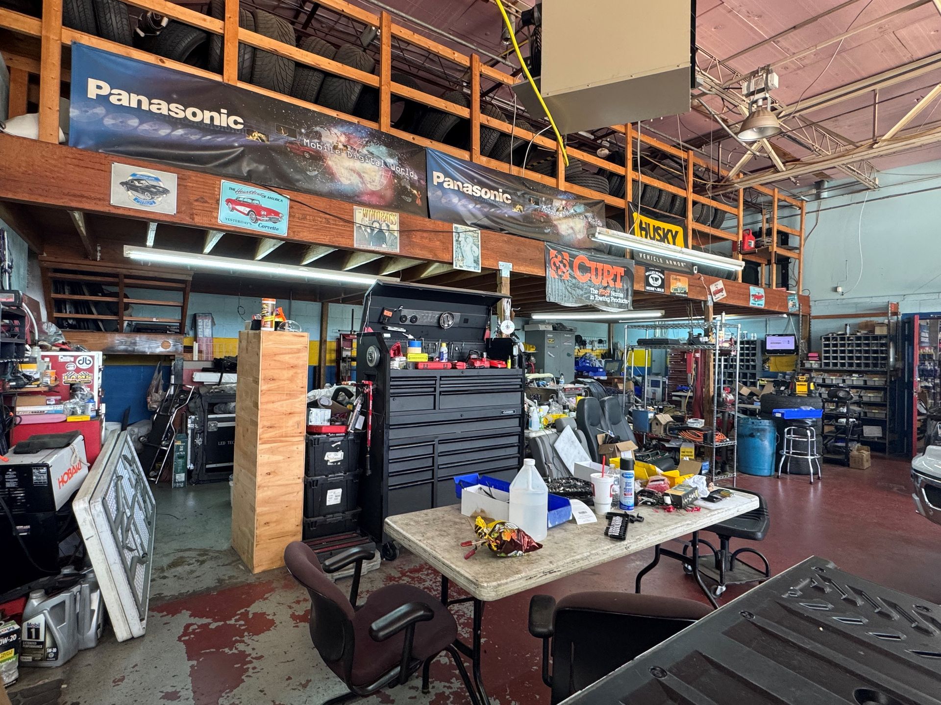 Auto repair shop interior with tools, car parts, shelves, and a workbench under an orange mezzanine.
