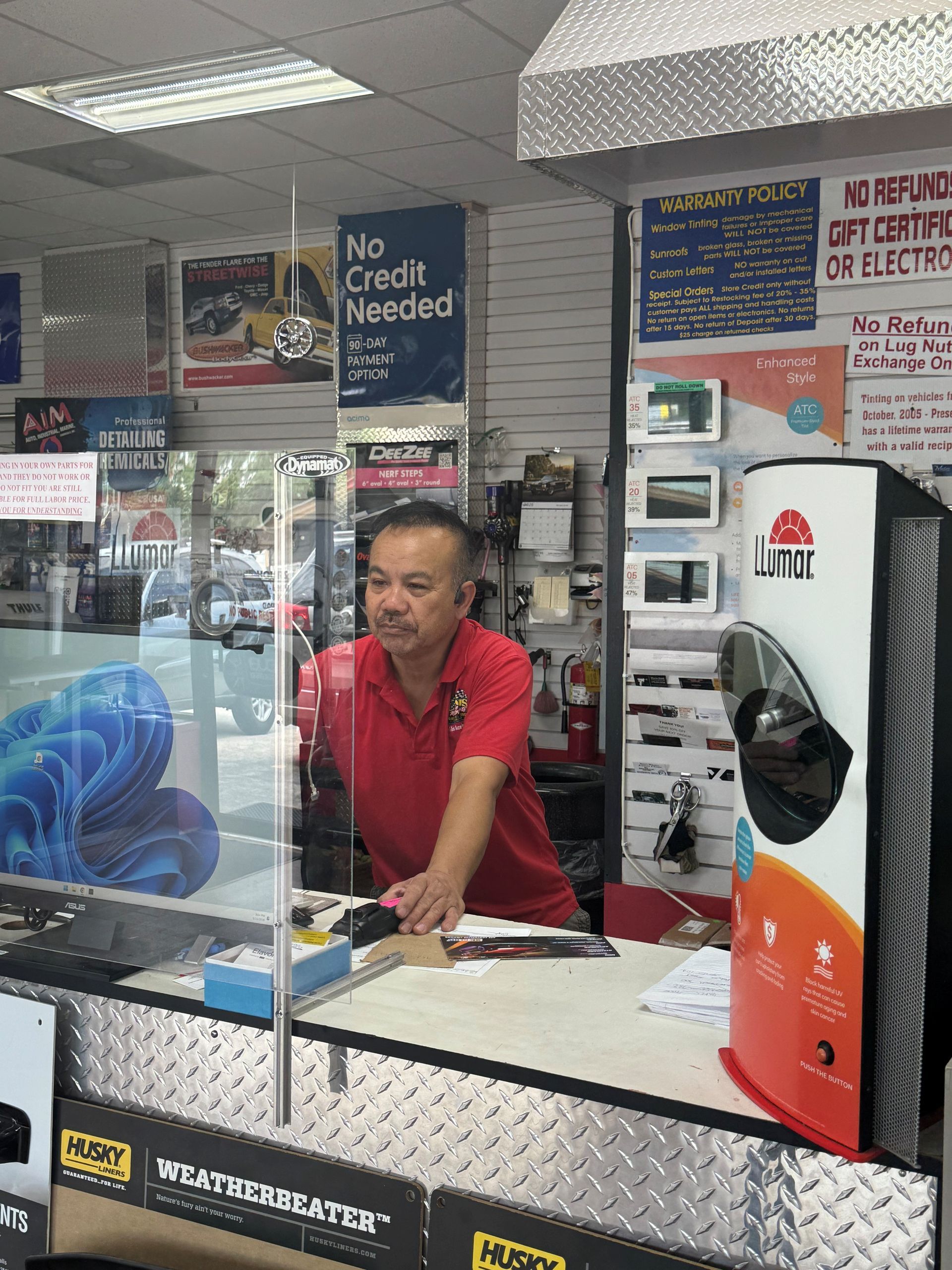 Man in red shirt working behind a counter in a small electronics or repair shop