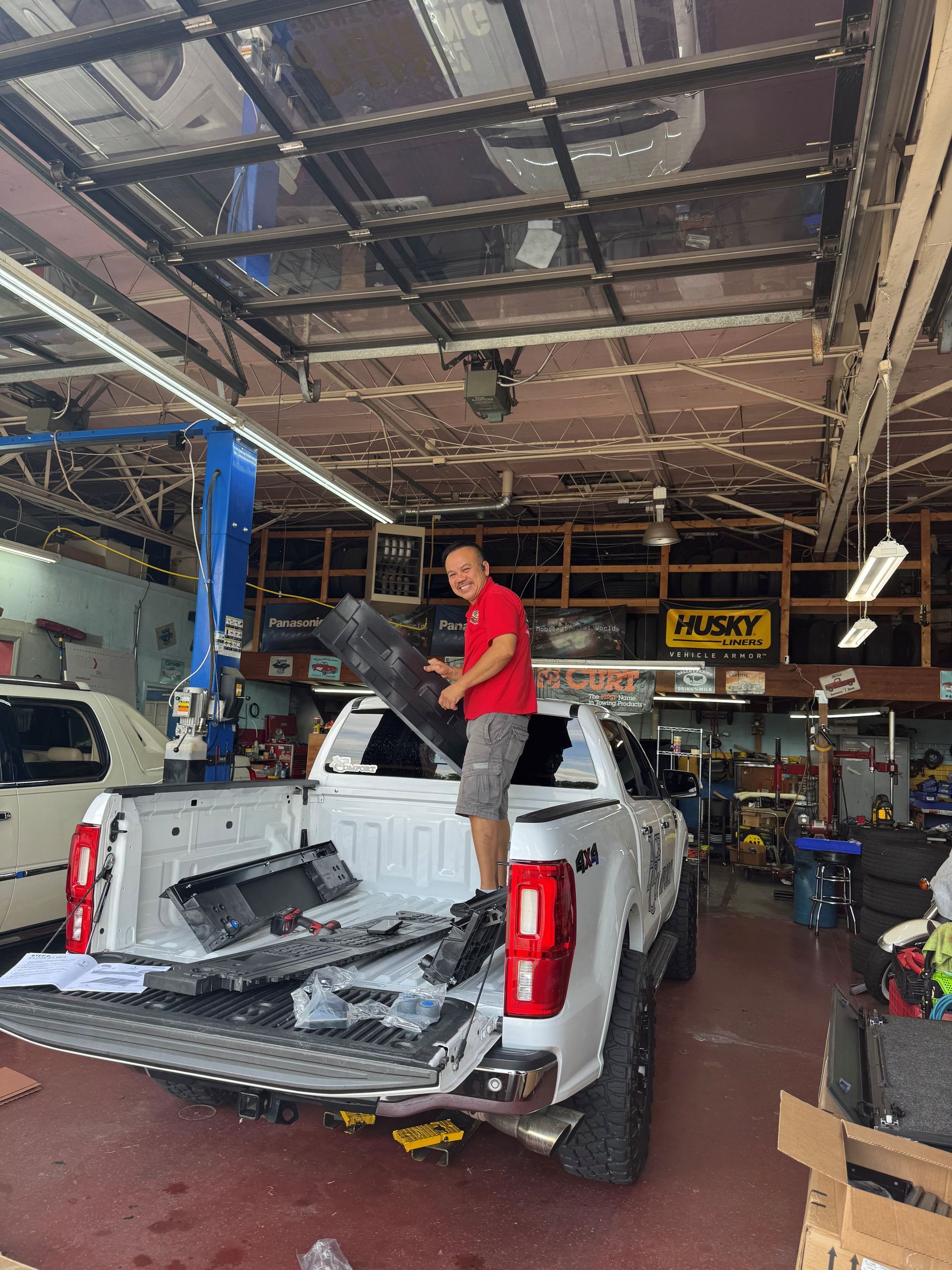 Person standing in the bed of a white pickup truck inside a garage, working on it