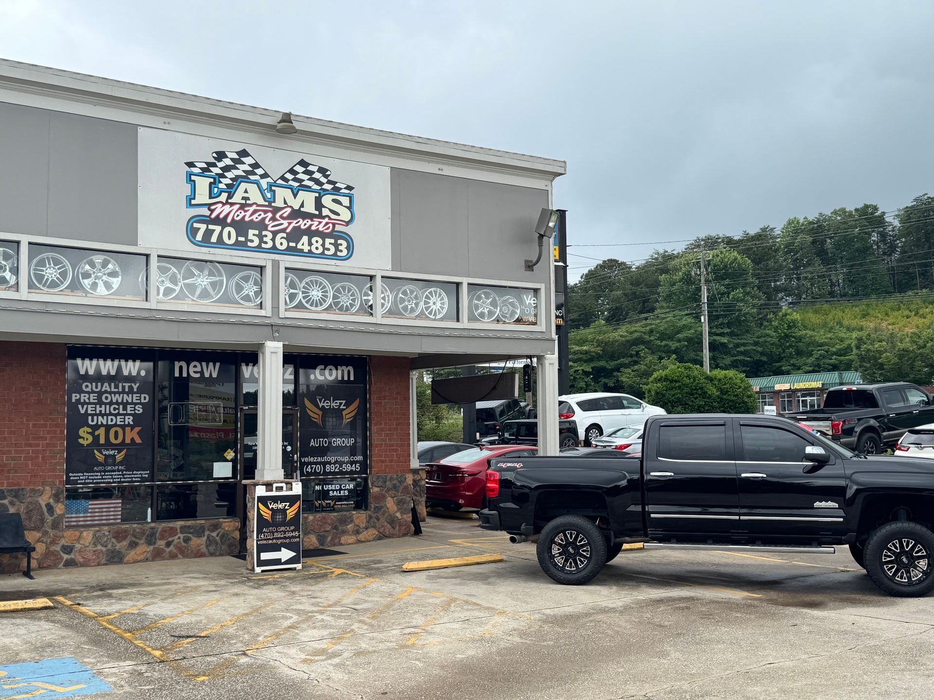 Black pickup truck parked outside a small storefront with a sign and cloudy sky behind it