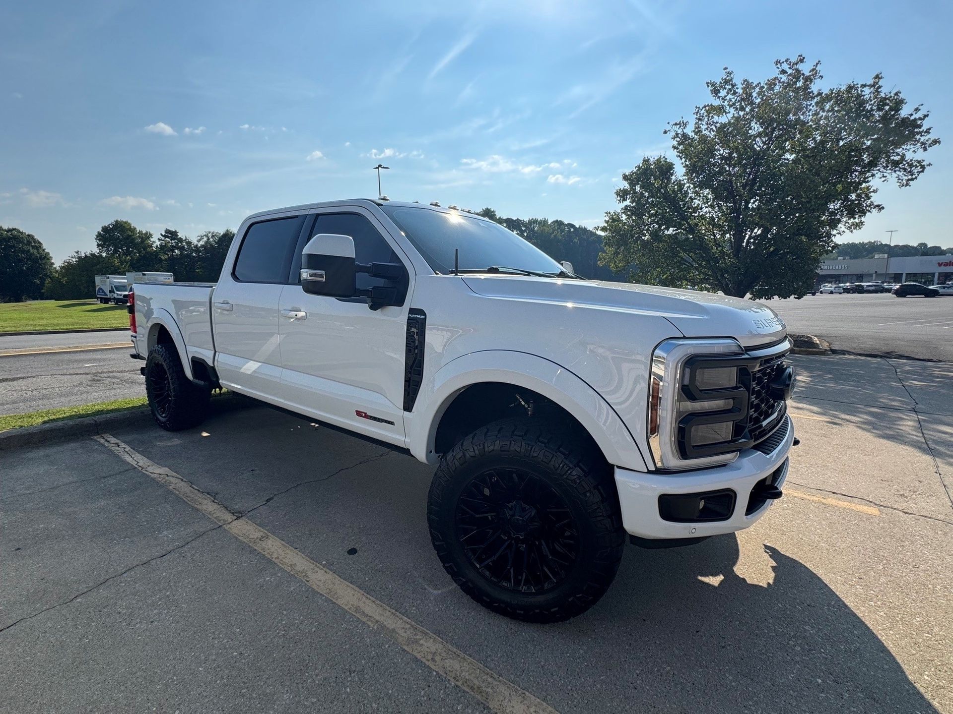 White lifted pickup truck parked in a lot under a blue sky