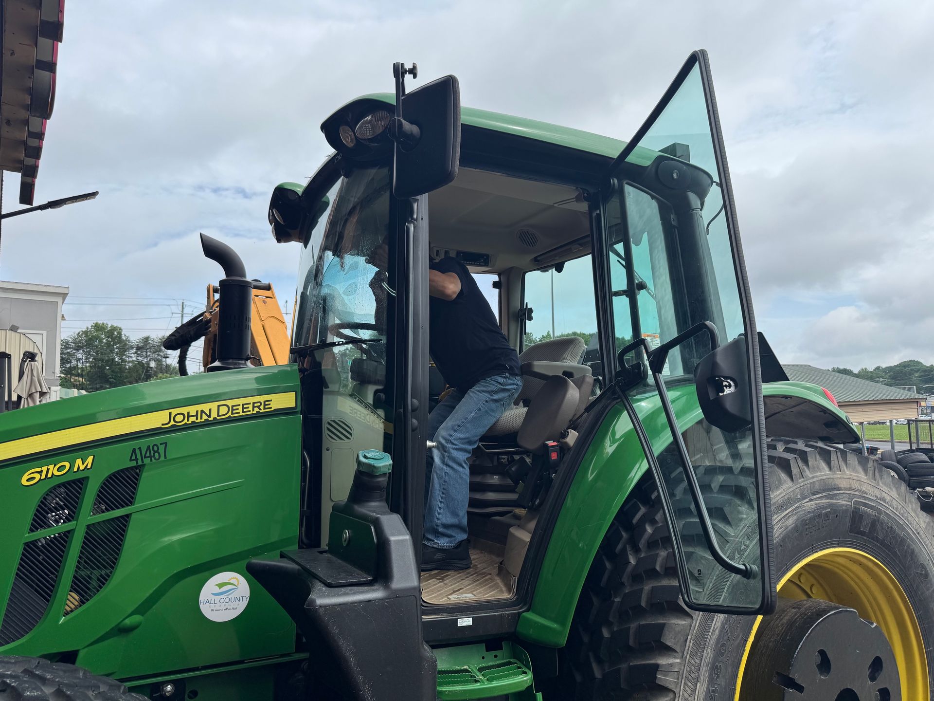 Green John Deere tractor with open cab and a person seated inside on a cloudy day