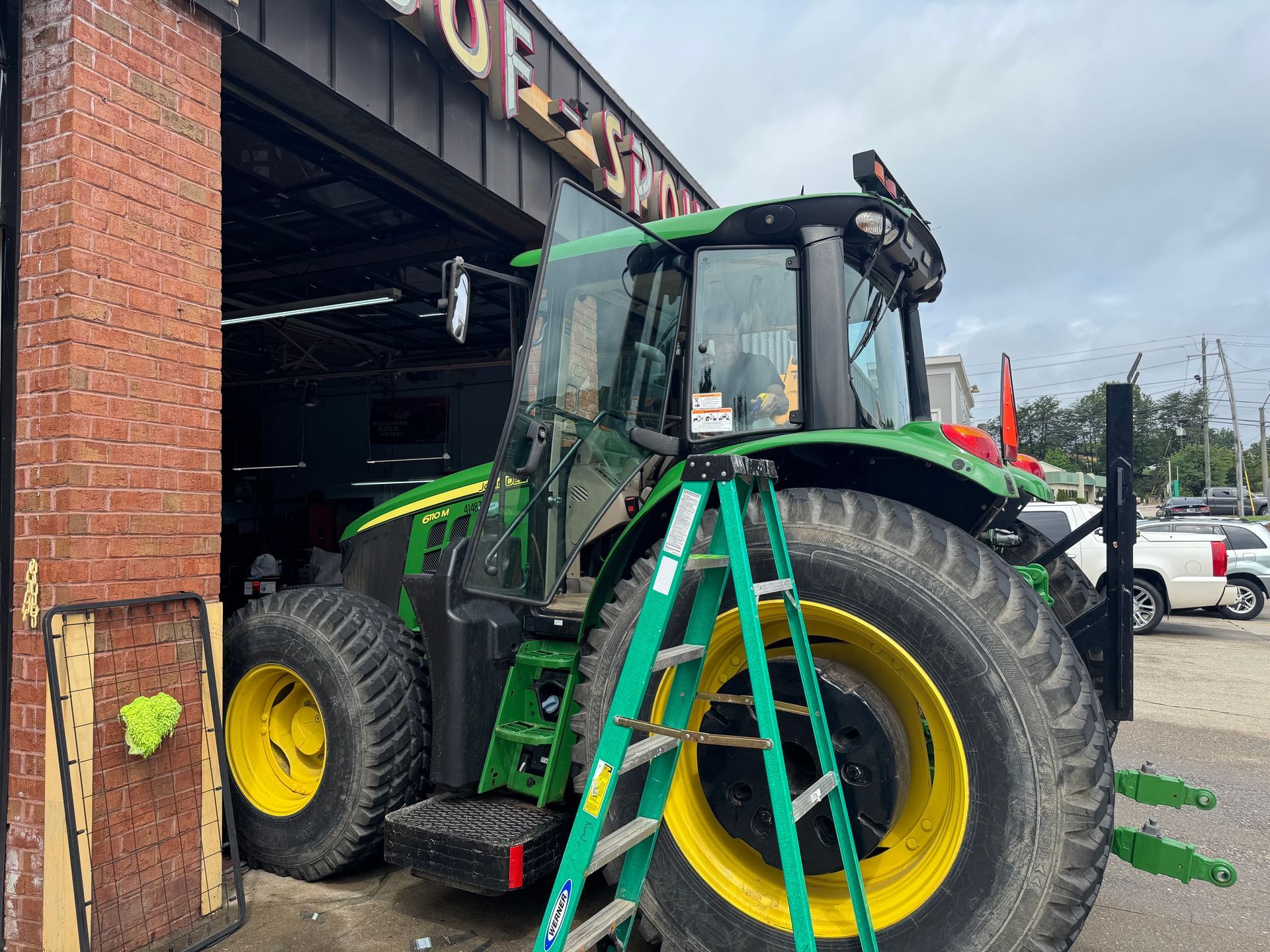 Green tractor with yellow wheels parked at a garage entrance, using a green ladder beside it.