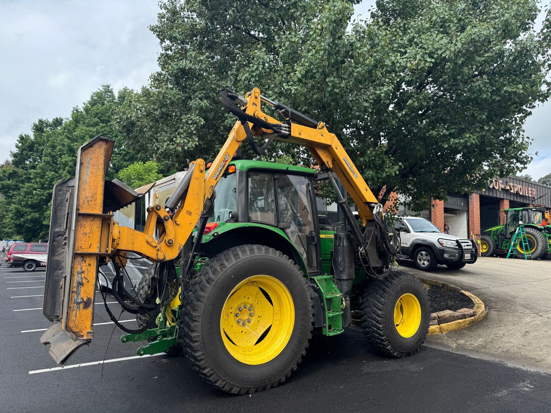 Green tractor with front loader parked outdoors near trees and other equipment