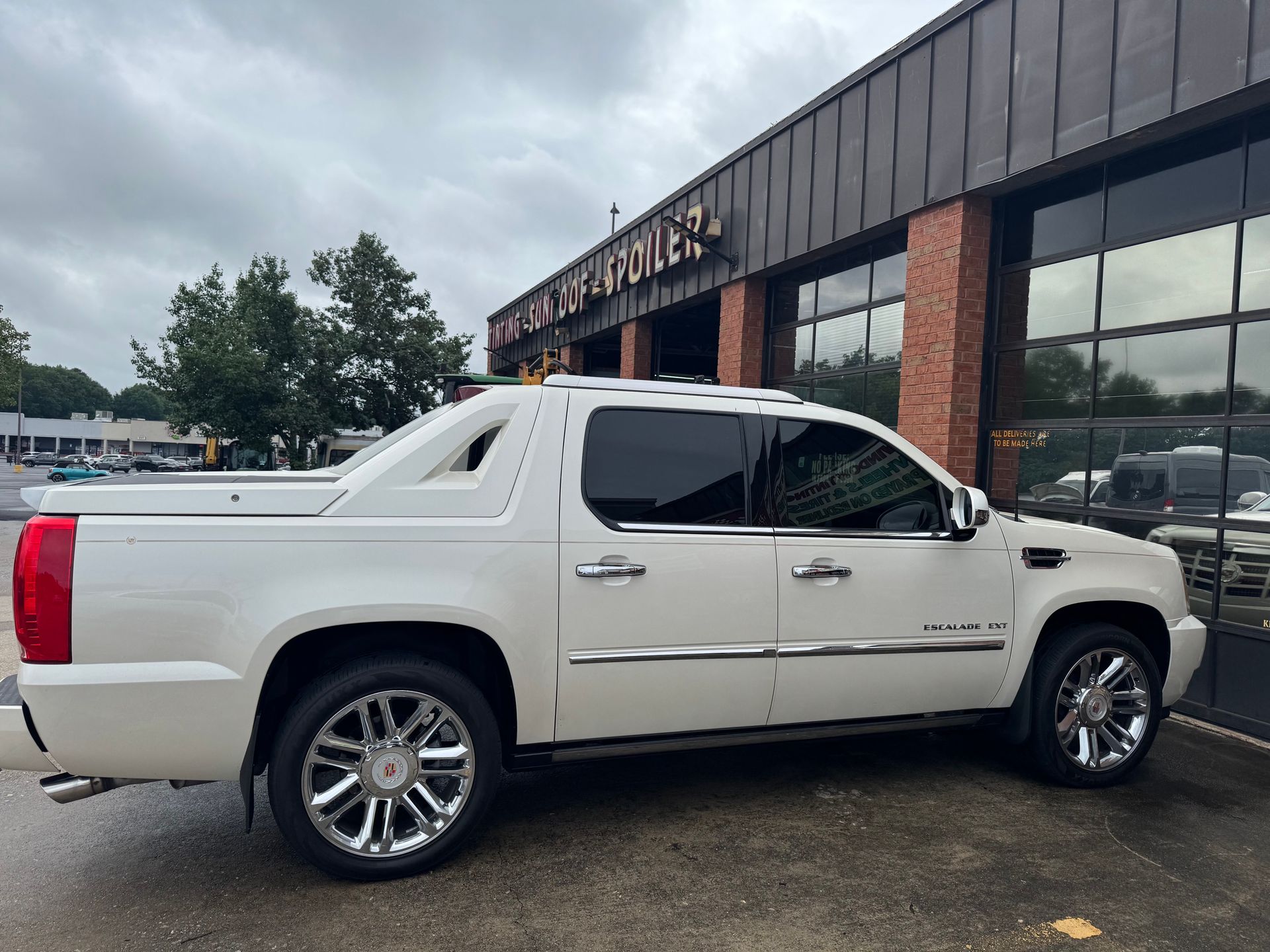 White pickup truck parked outside a storefront on a wet pavement, side view.