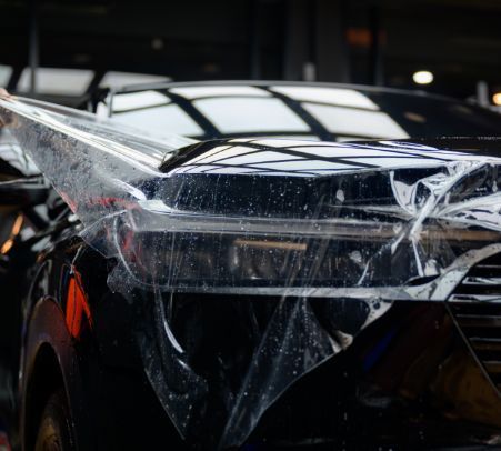 Damaged car hood with shattered windshield and peeling protective plastic cover