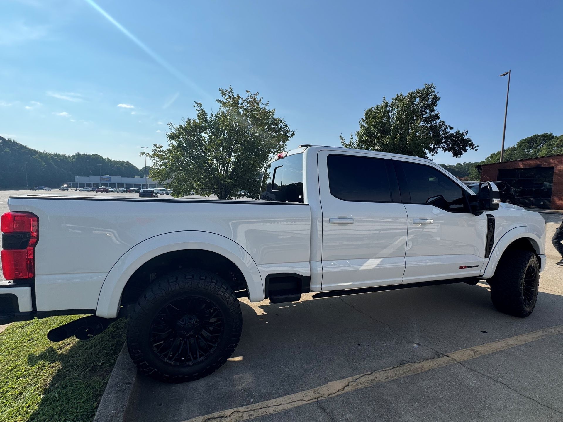 White lifted pickup truck parked in a lot beside water, under a clear blue sky.