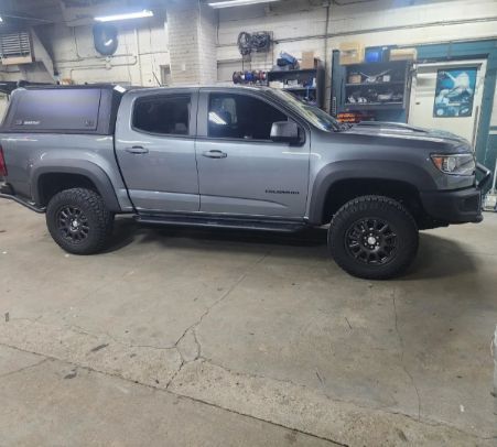 Gray pickup truck parked inside a garage or auto shop with concrete floor and shelves in the background