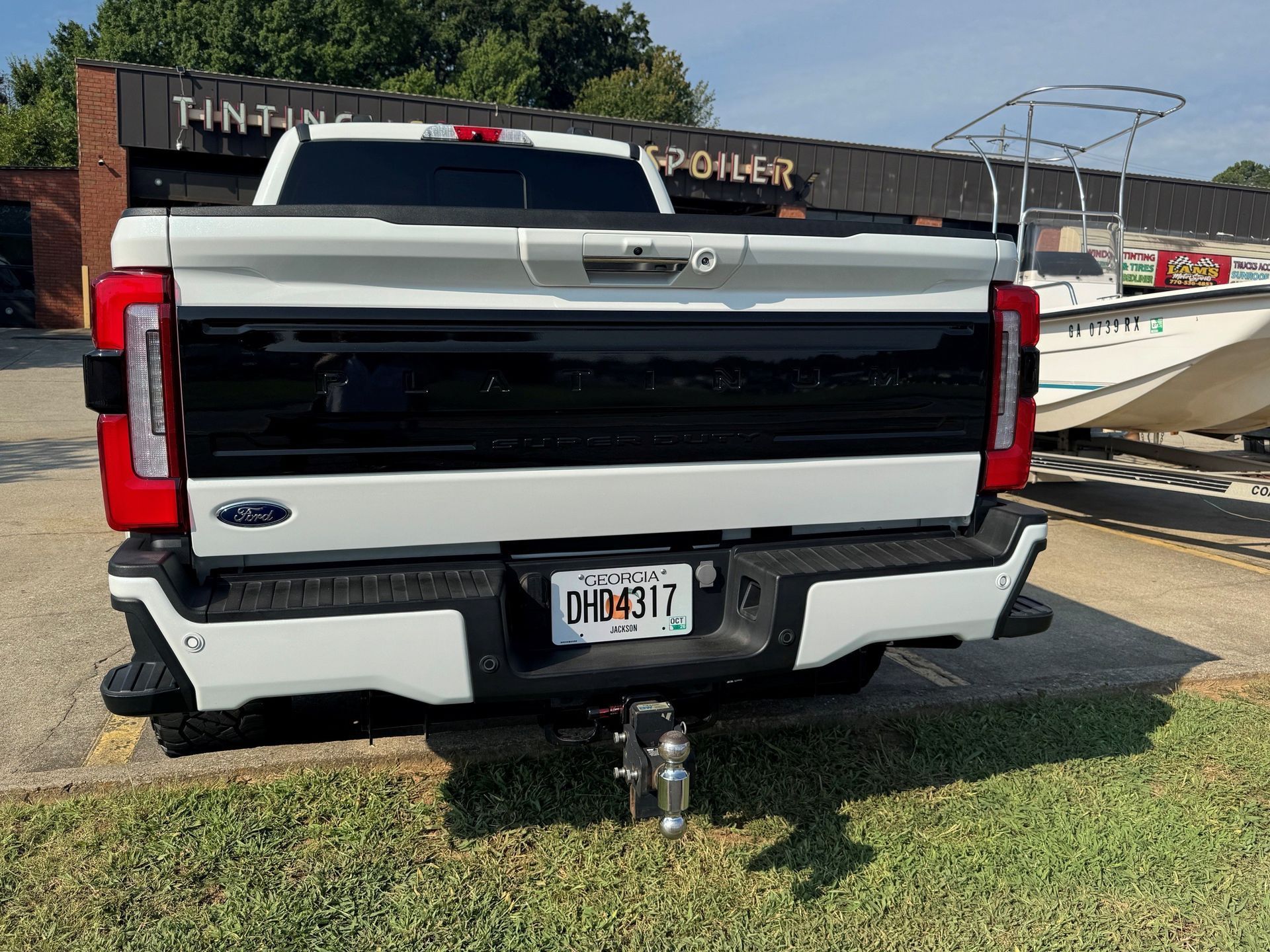 Rear view of a black-and-white pickup truck parked on grass near a boat trailer, with a hitch attached.