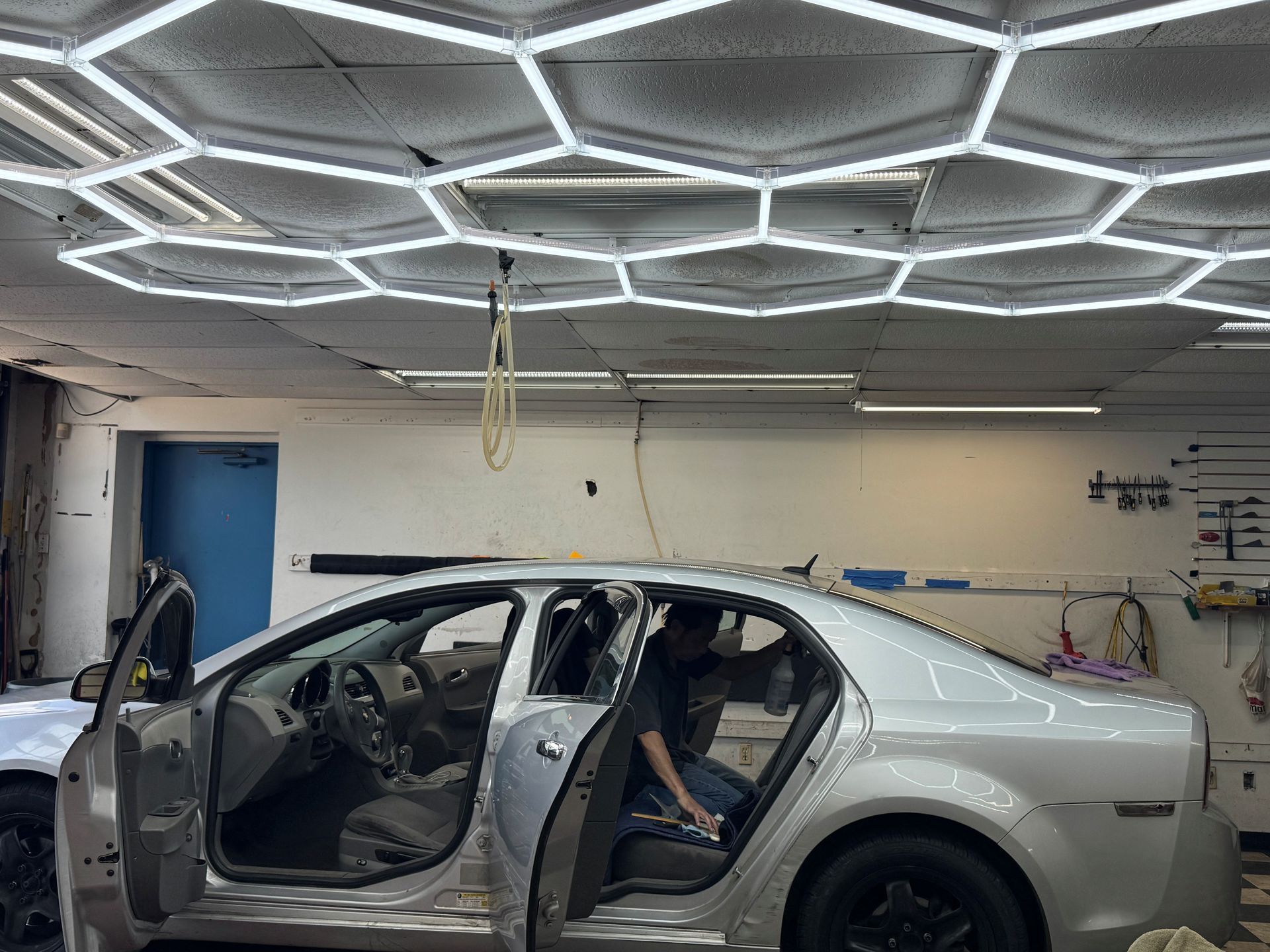Car stripped for repair in auto shop with LED ceiling lights and a person inside the back seat