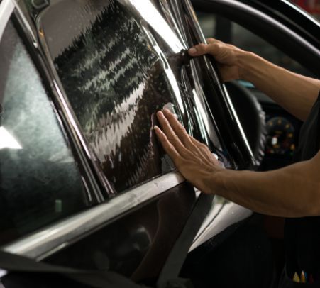 Hands polishing a black car window with a cloth, reflected in the glossy surface