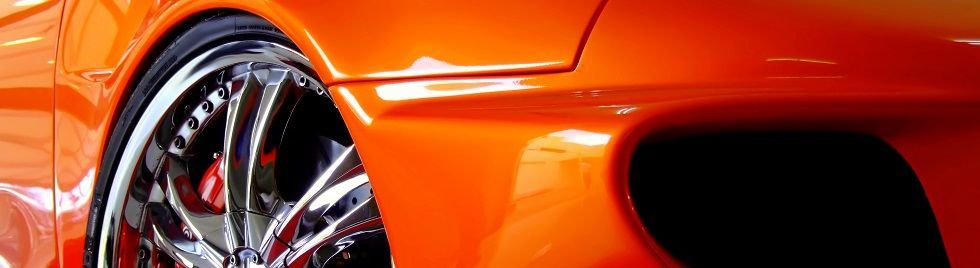 Close-up of an orange sports car’s chrome wheel and front bumper detail
