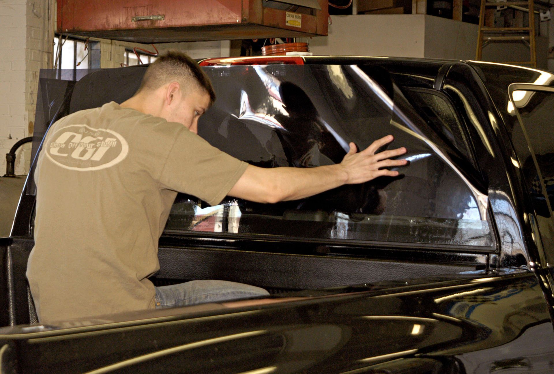 Man polishing the rear window of a black car in a garage