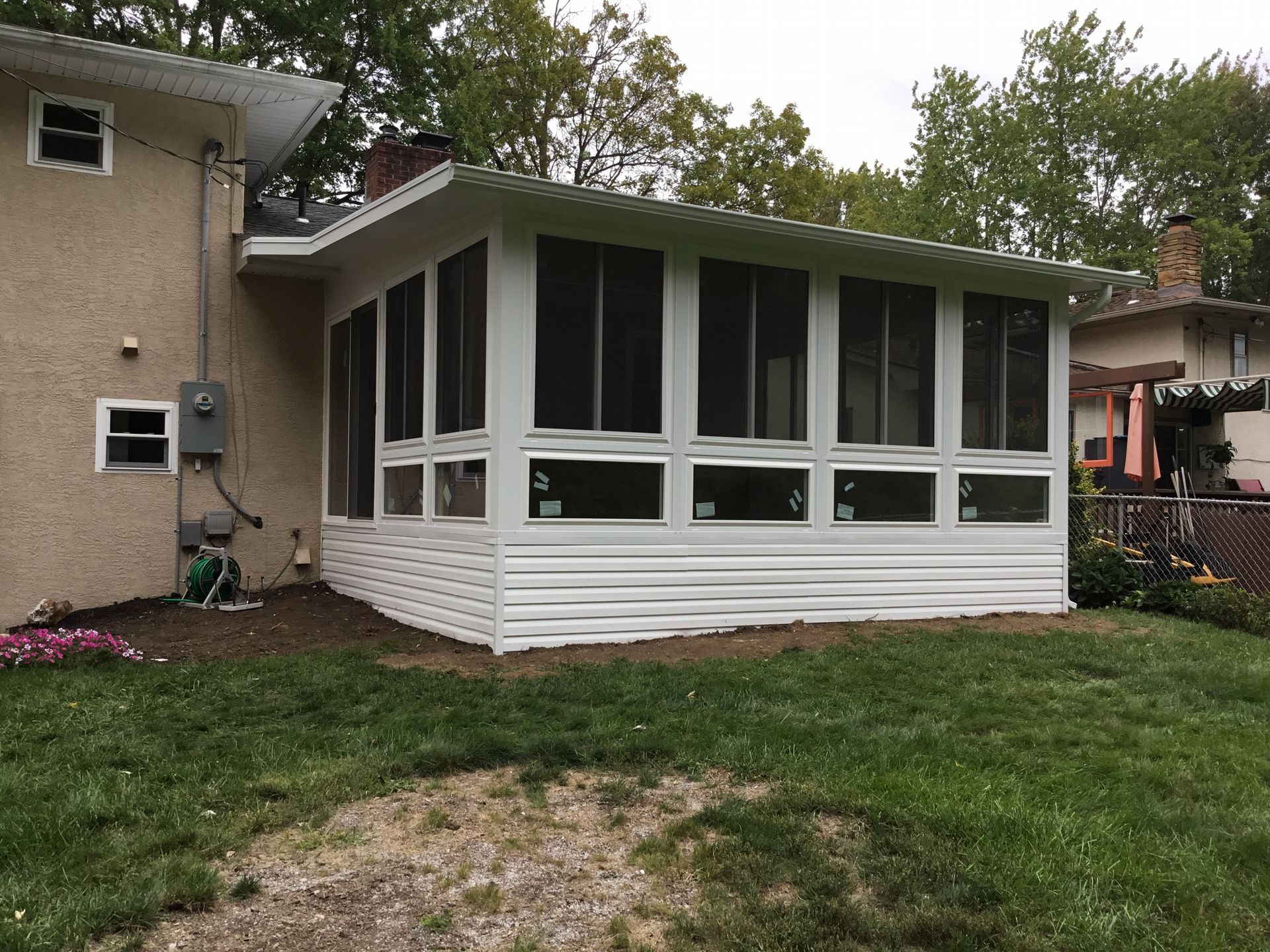 White screened-in porch addition attached to a beige house, overlooking a grassy yard.