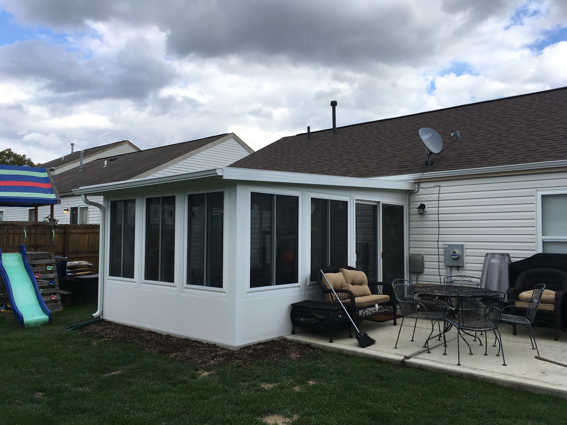 White screened-in porch attached to a house with outdoor furniture on a patio and a green lawn.