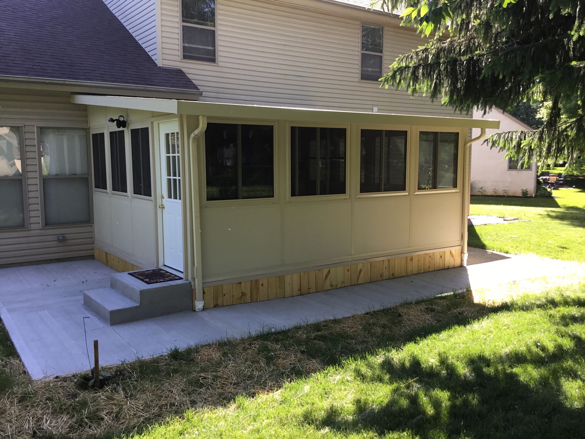 Screened porch with concrete patio attached to a two-story house, set in a grassy yard.