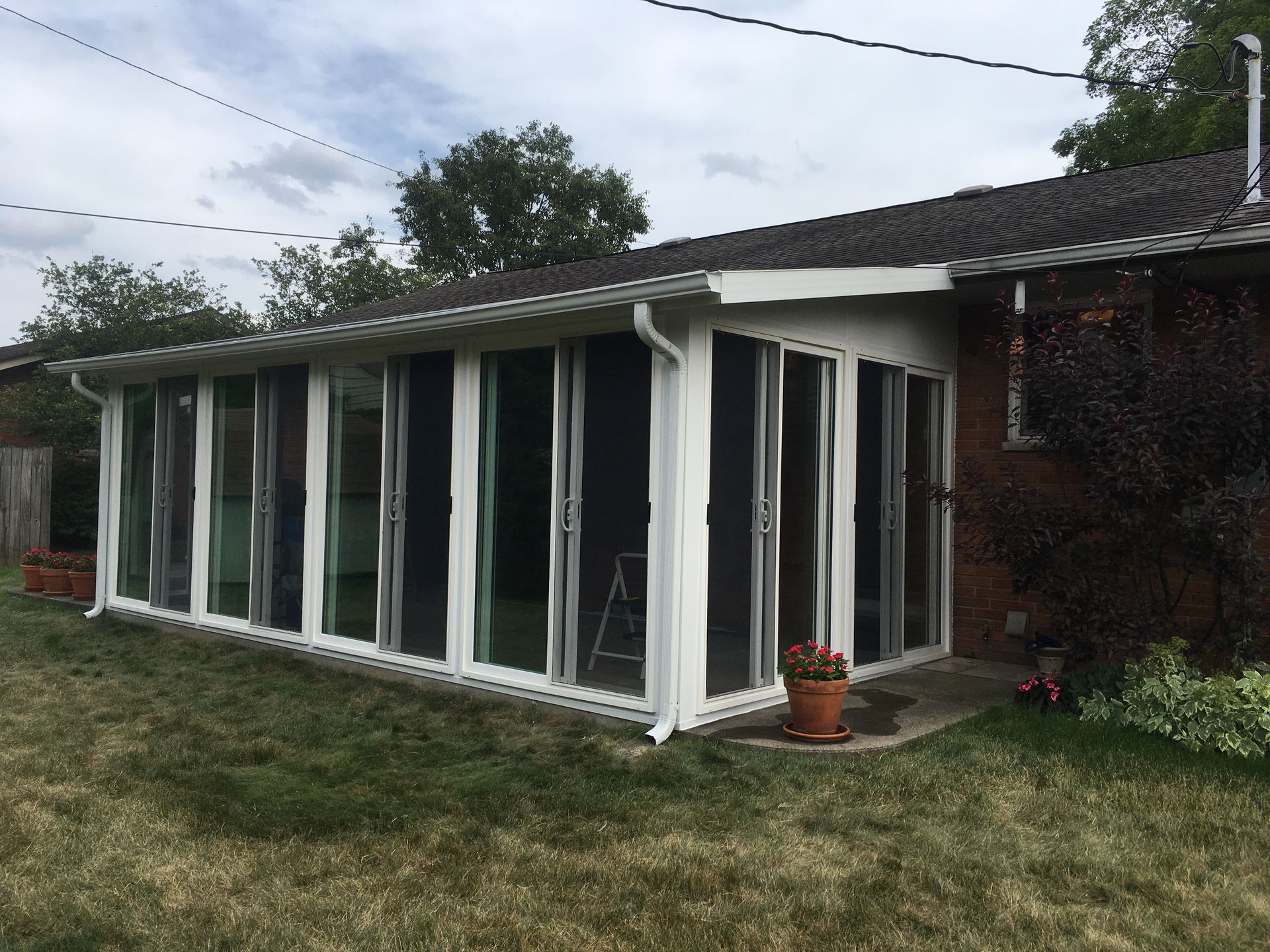 Sunroom addition with white frames and sliding glass doors, attached to a brick house.