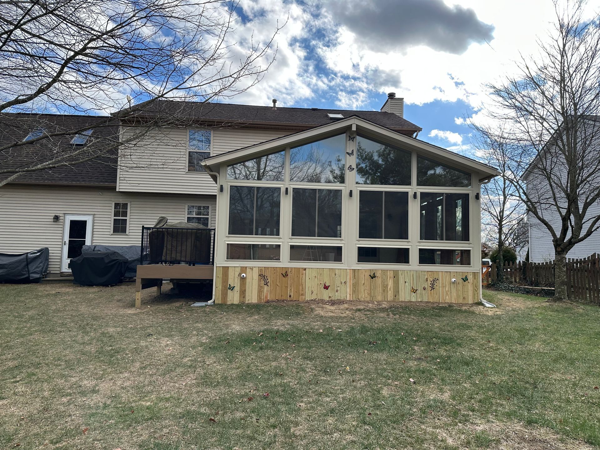 A two-story house with a screened porch attached. The porch has a wooden base and glass windows.