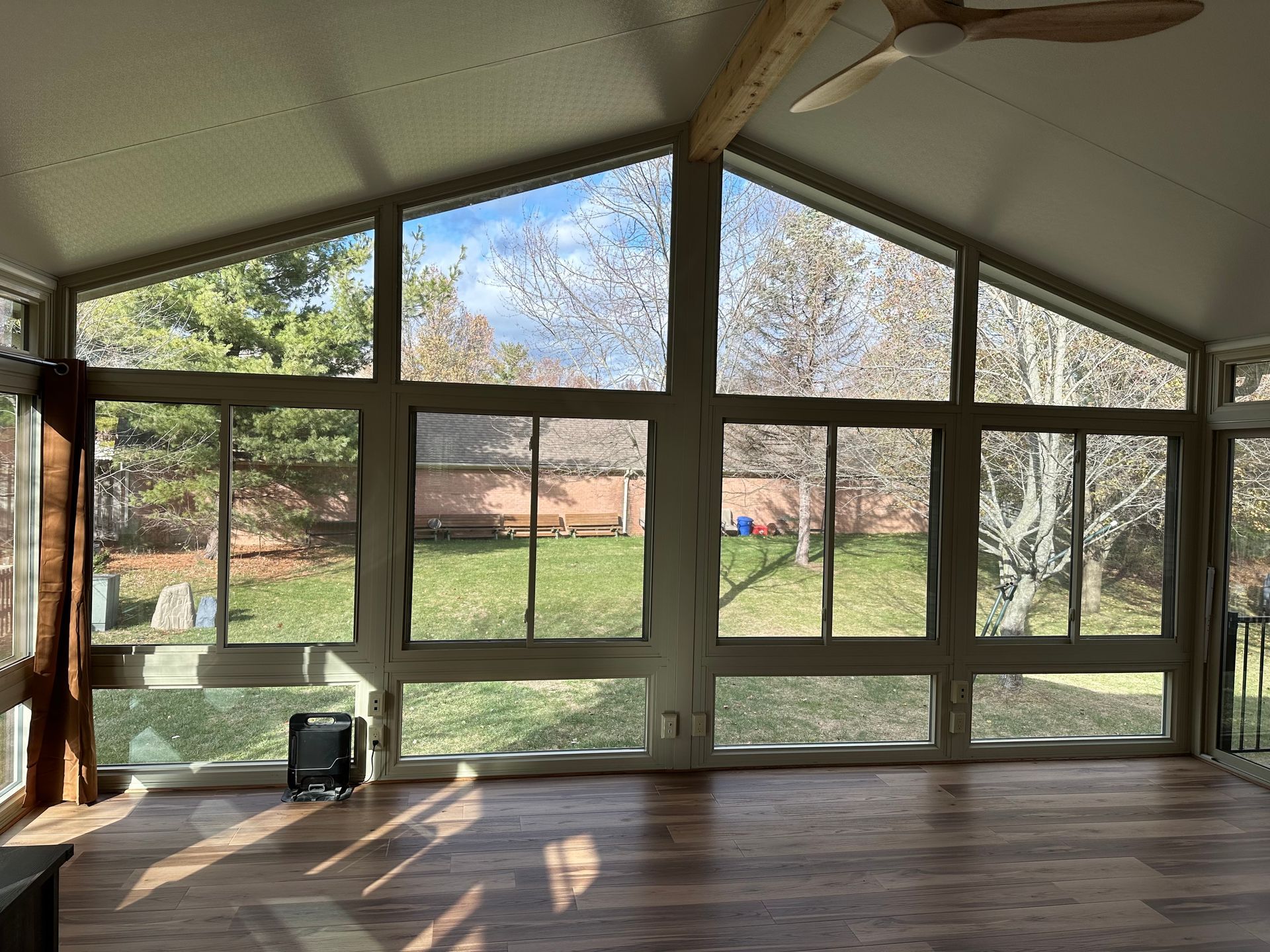 Sunroom with large windows overlooking a backyard with trees and grass. A ceiling fan is visible.