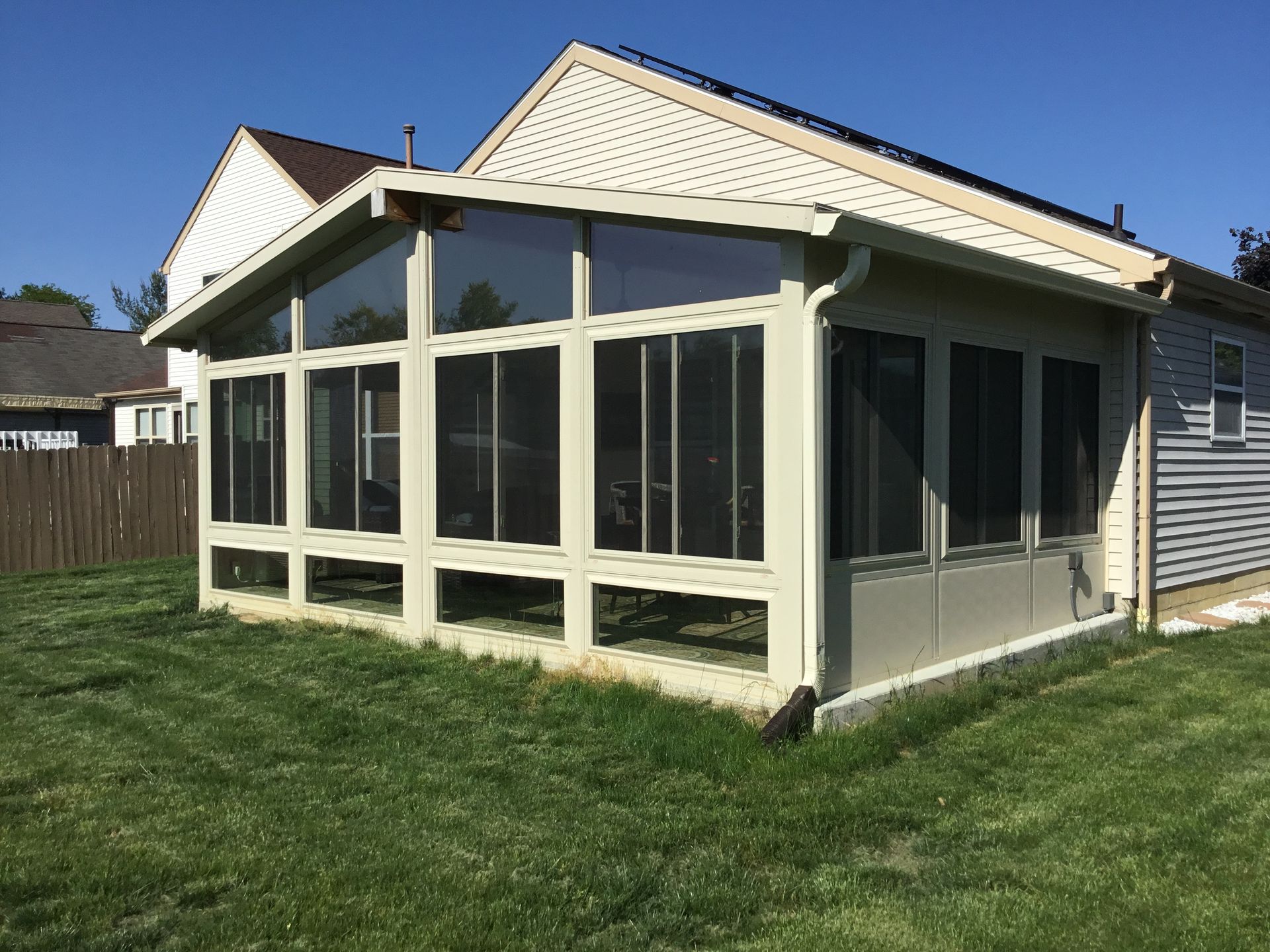 Beige sunroom addition with glass windows and screen panels, attached to a house with a grassy lawn.