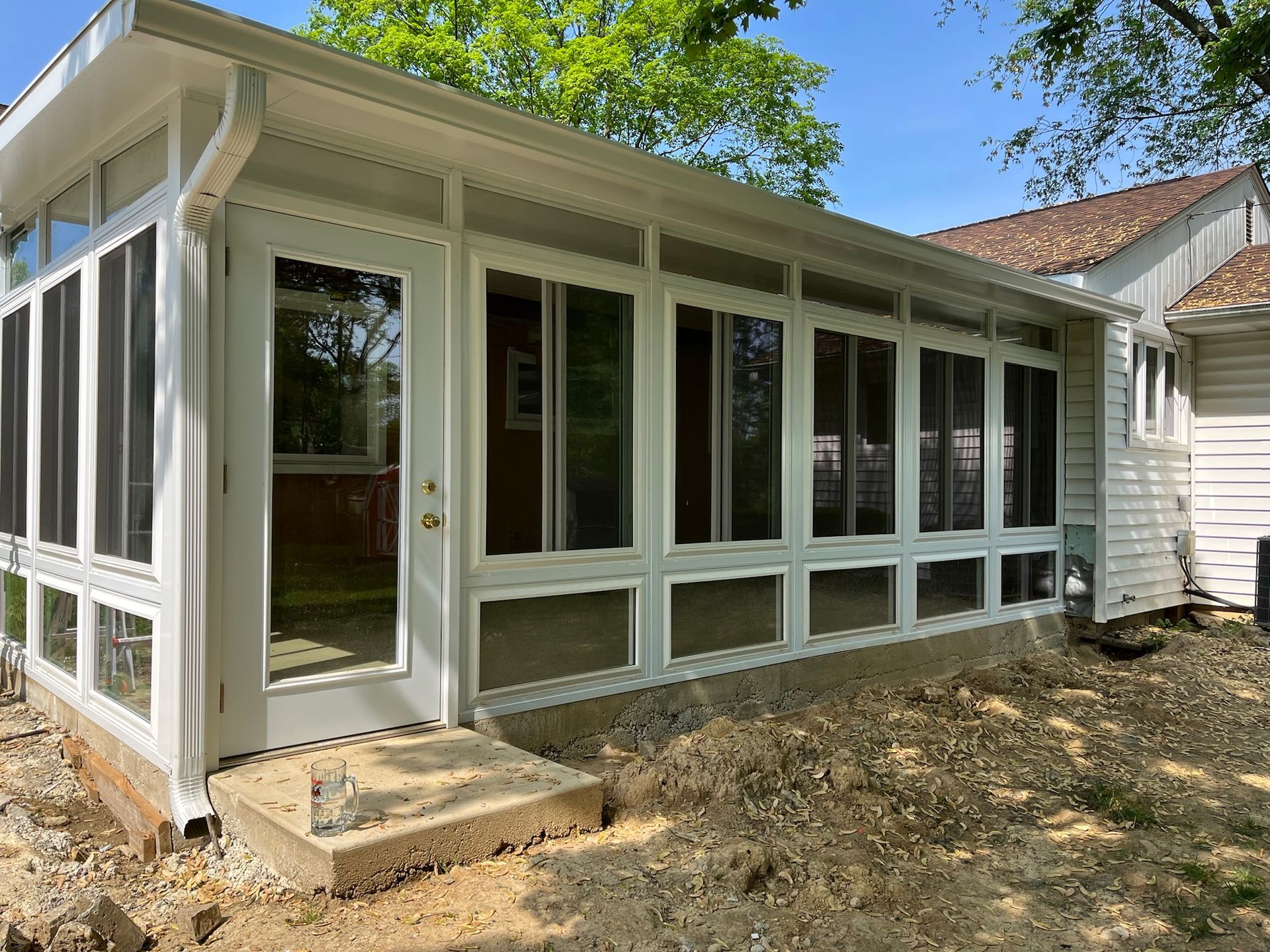 White-framed sunroom with glass windows and screens, attached to a house with a brown roof.