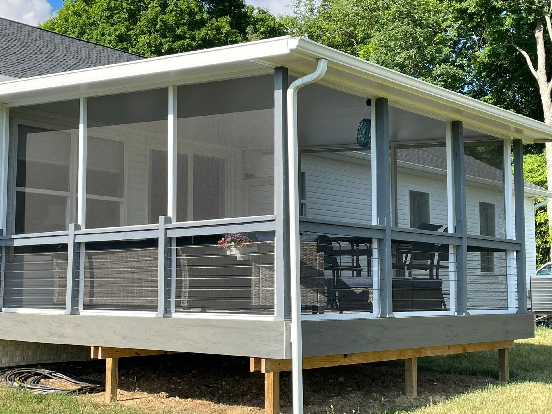 Screened-in porch on a raised deck with gray trim and white siding, in a backyard setting.