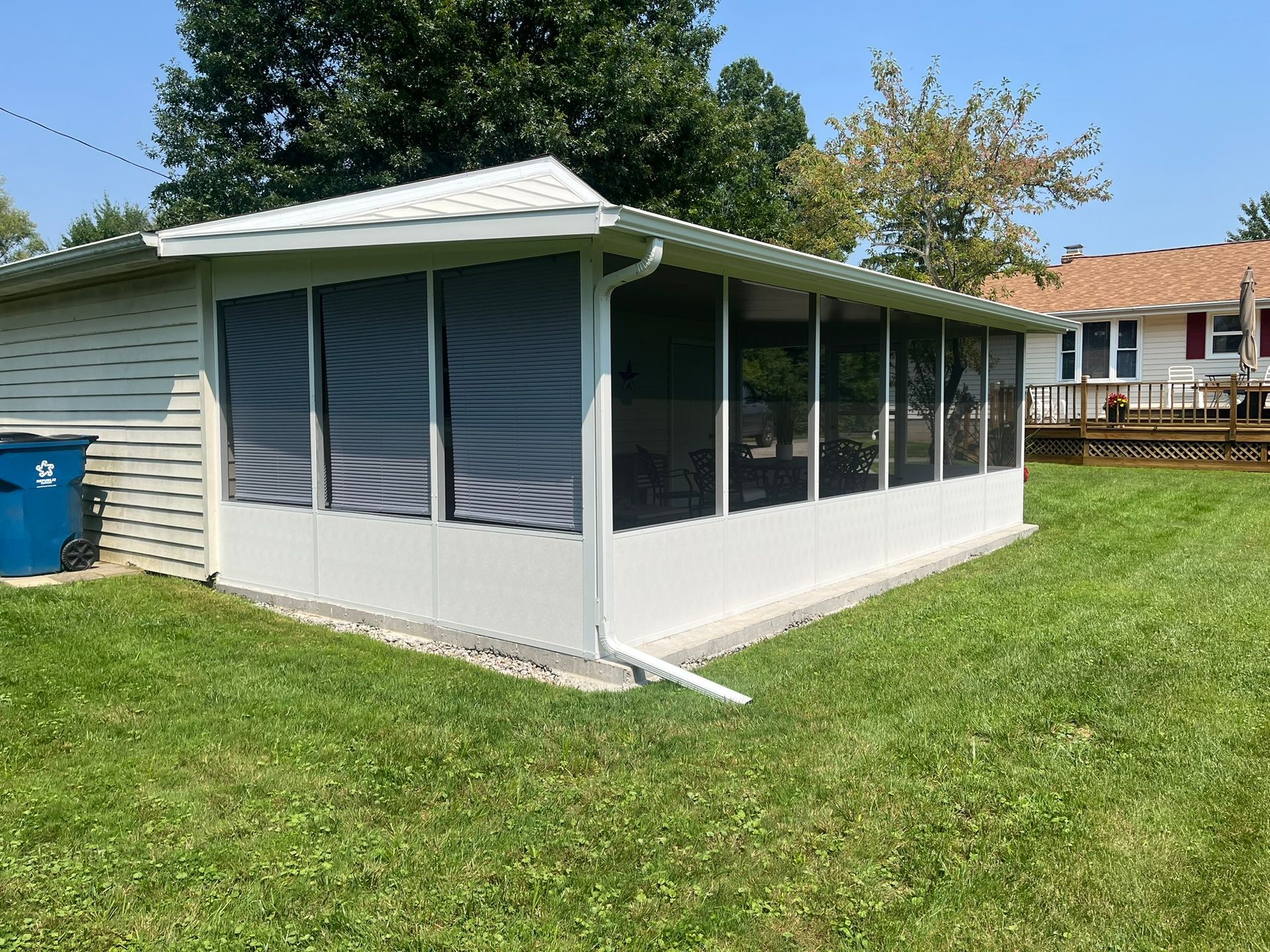 White screened porch attached to a white-sided house with a green lawn.
