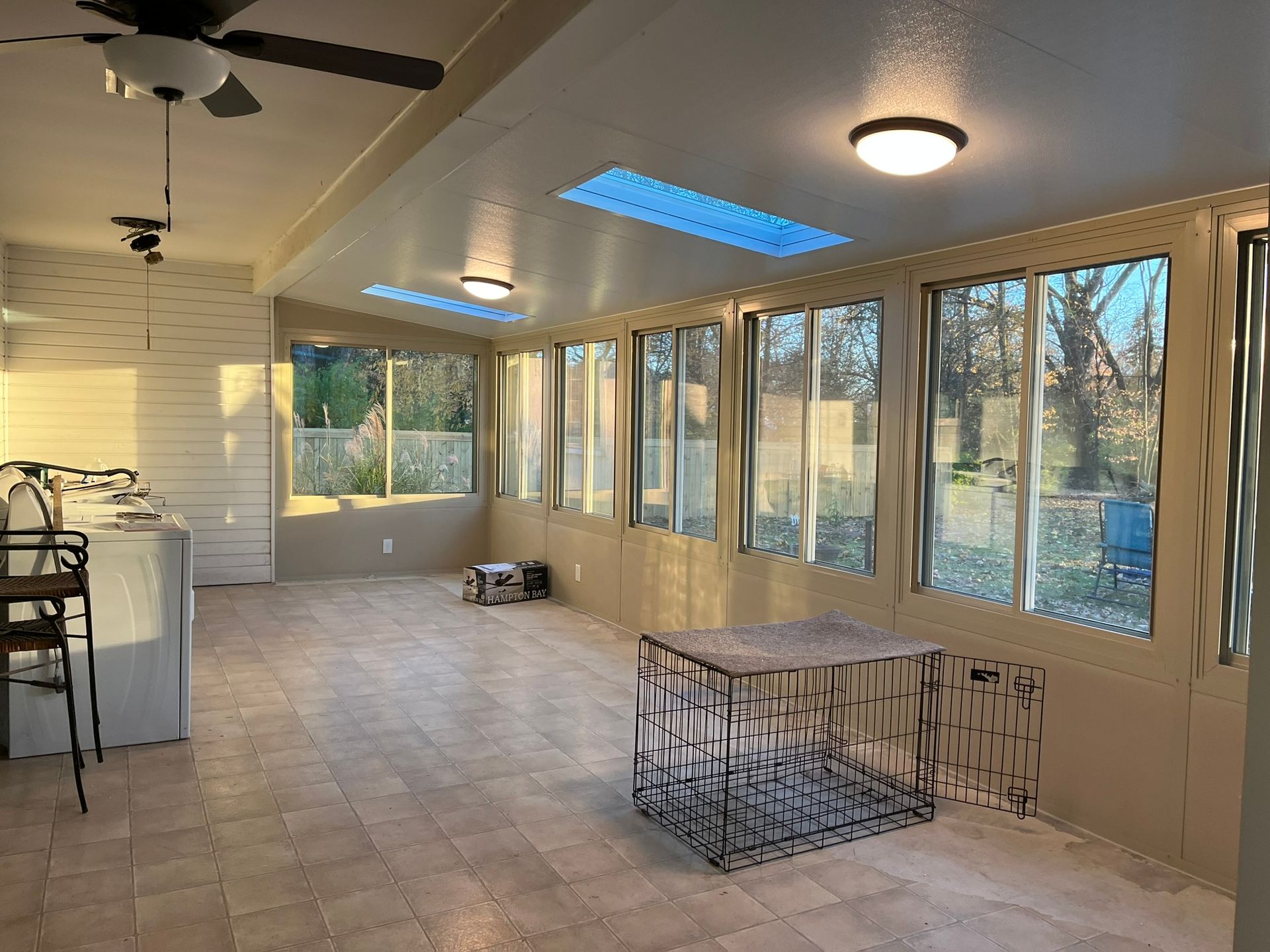 Sunroom with large windows, skylights, and tiled floor. A metal dog crate sits in the center.