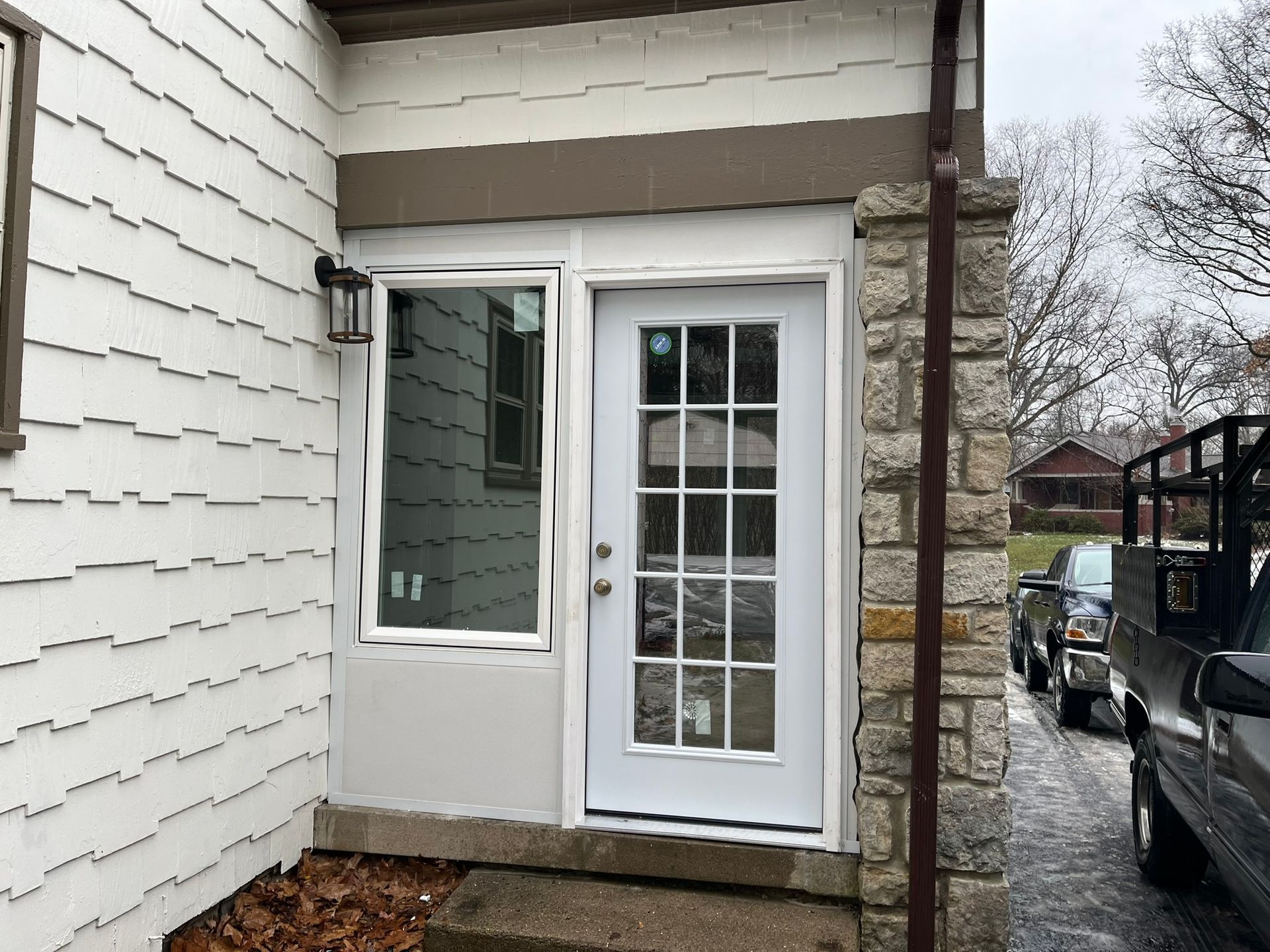 Exterior door and window on a house with a stone column and a truck parked nearby.