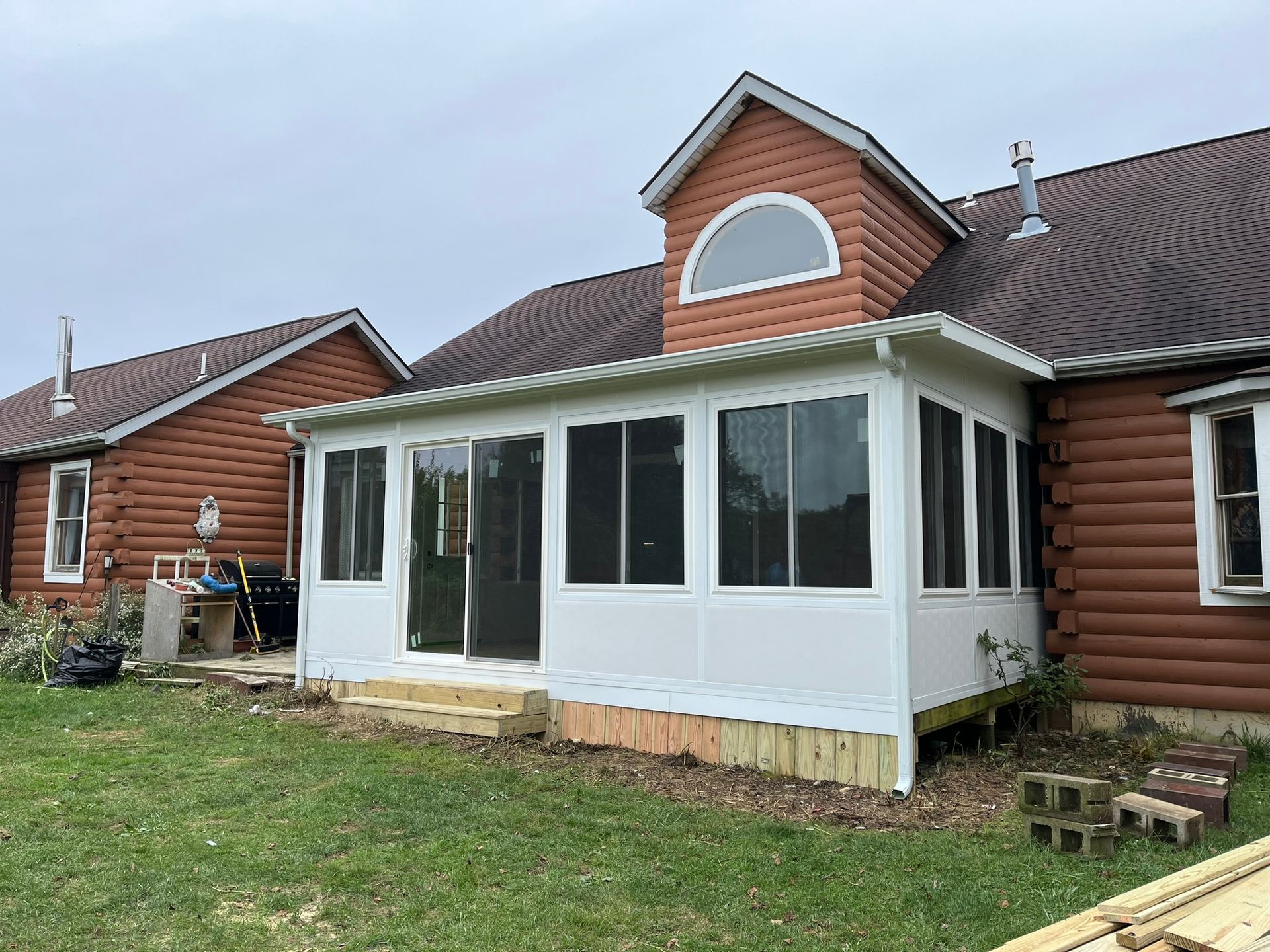 White framed sunroom addition with glass and screen windows on a brown log-sided house.